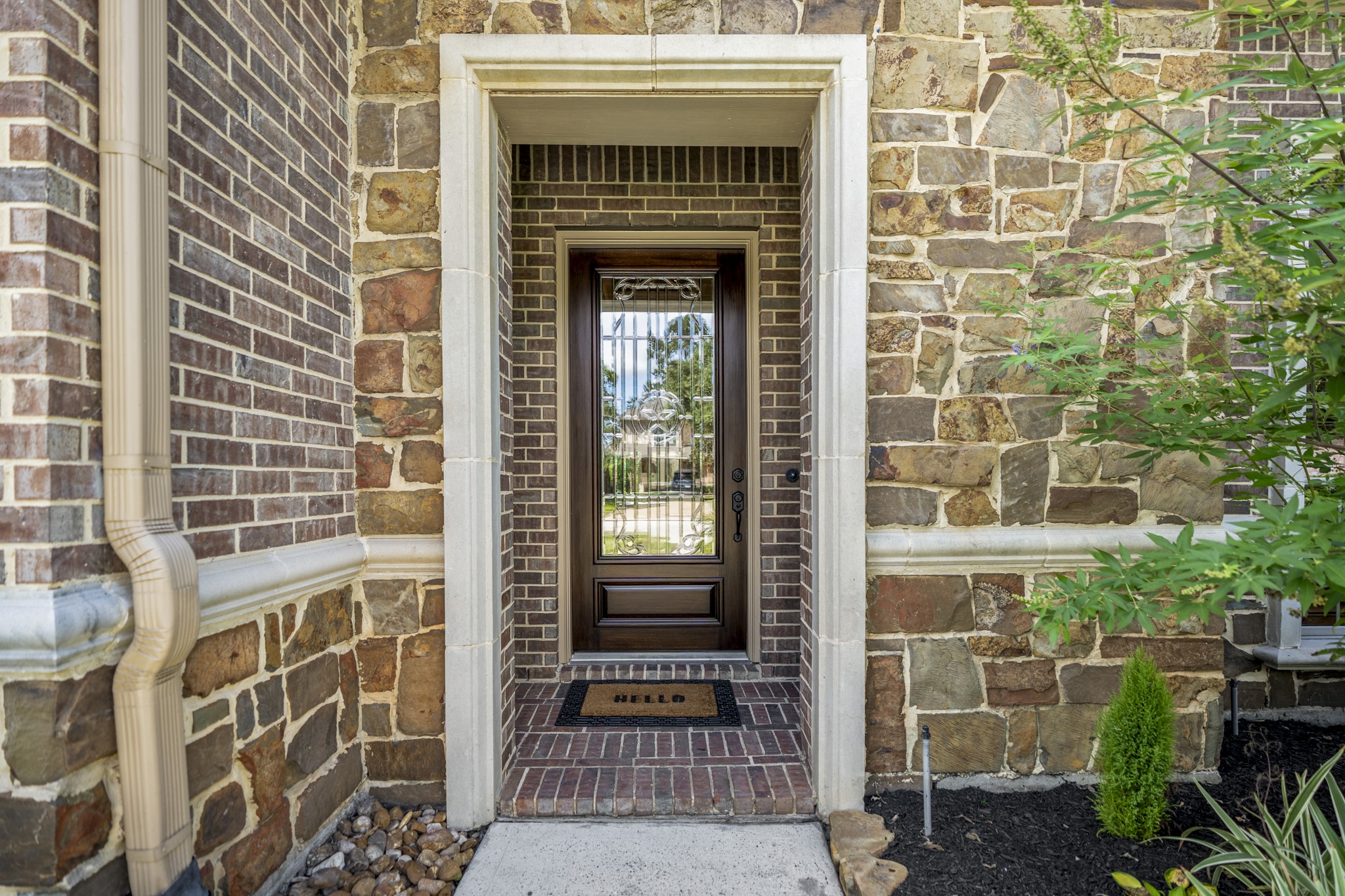 At the front entry, brick-and-stone detailing, a recessed porch, and a decorative glass door with Texas star detailing create a polished welcome into the home. This close-up gives buyers a first feel for the homes elevated exterior finishes before the walkthrough moves inside.