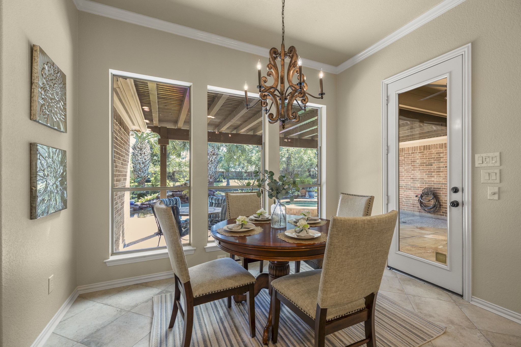 Breakfast nook sits just beyond the kitchen, wrapped in windows that draw in natural light and keep the poolside, water-front backdrop in view. The glass door on the right opens to the covered outdoor living area, making this an easy spot for morning coffee before heading out toward the pool, spa, and backyard beyond. Along the left side, the hallway leads to two secondary bedrooms and a full bath.