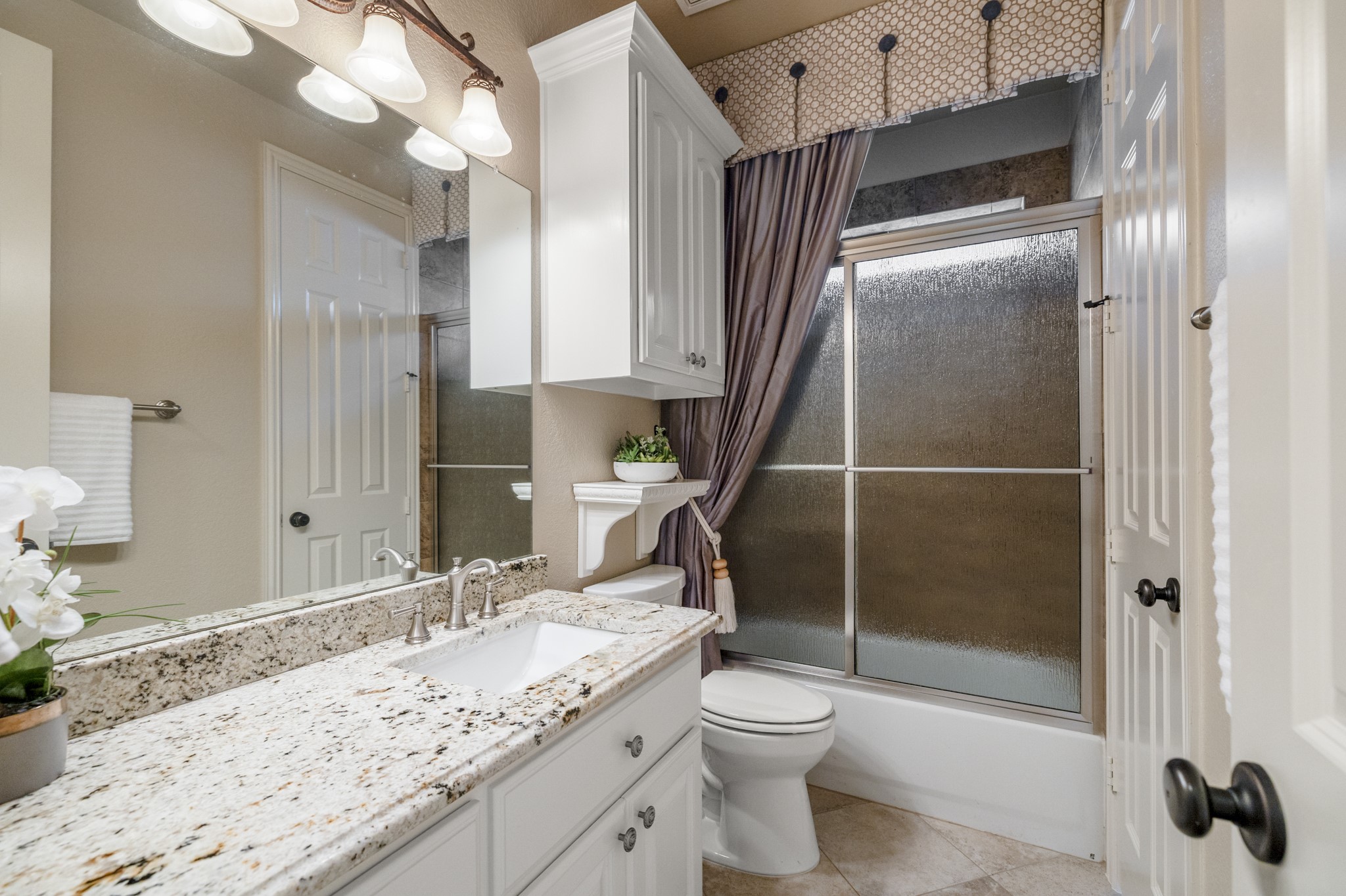 Serving the two rear secondary bedrooms, this bath keeps the back-of-home wing polished and convenient without pulling attention away from the homes main living spaces. The framed mirror, upgraded lighting, vanity storage, and tiled tub/shower surround give the space a finished feel as the walkthrough continues between the nearby bedrooms.