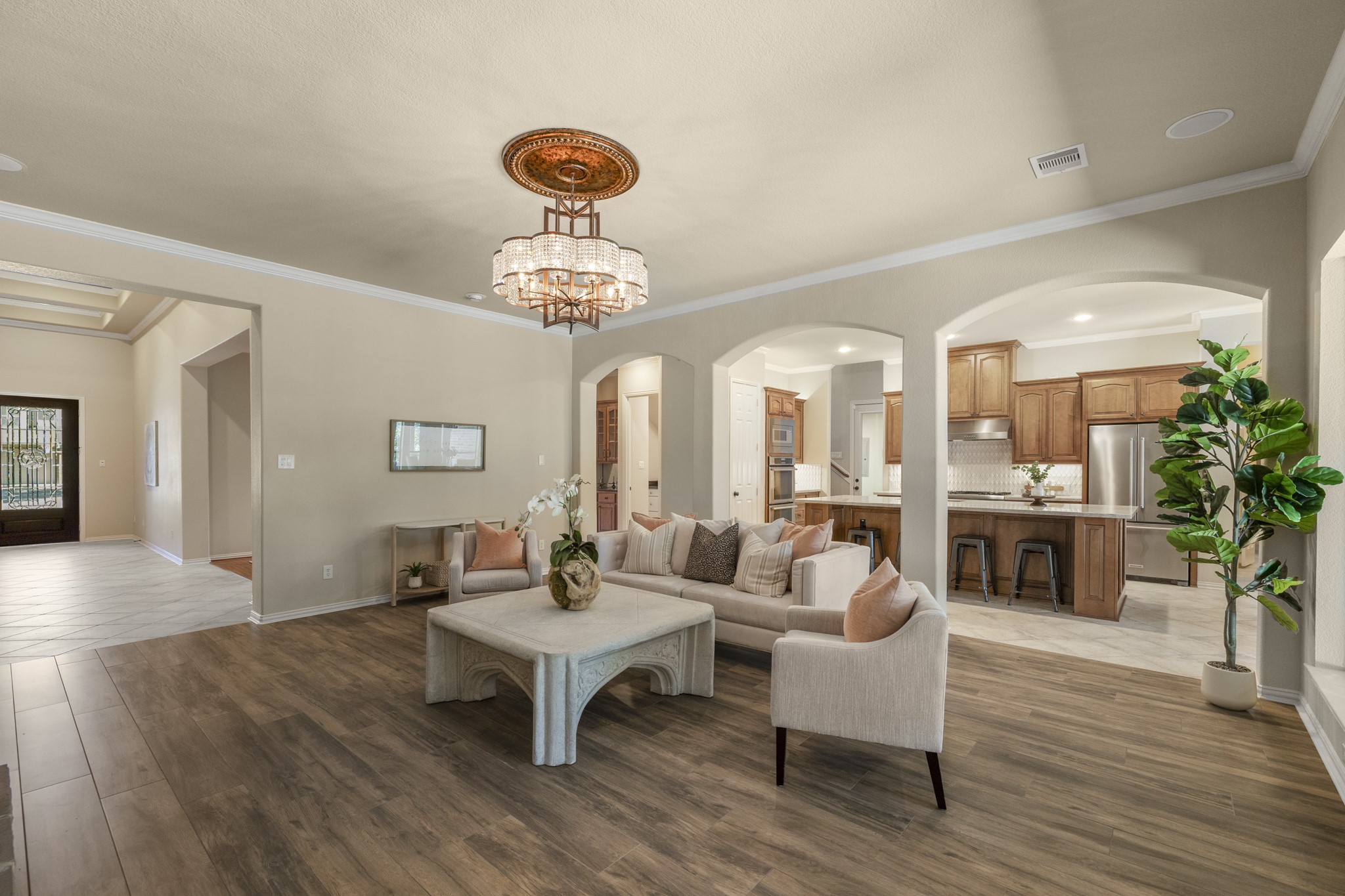 Pulled farther back, the living room shows how the main level gathers around one central space, with the kitchen open on the right and the fireplace framed by custom lighted built-ins ahead. The view keeps the homes entertaining flow easy to follow, connecting the kitchen, breakfast area, and living room before the walkthrough continues toward the poolside backyard and water-view setting beyond.