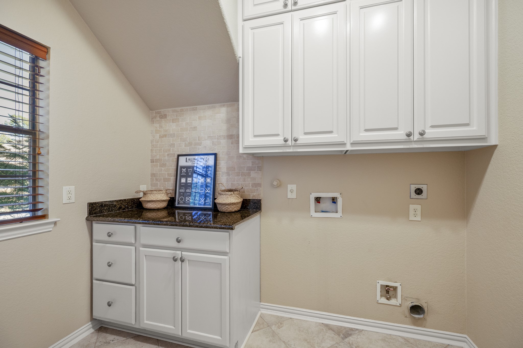 Positioned in the hallway between the dining room and kitchen, the utility room downstairs keeps laundry tucked close to the homes main living spaces without interrupting the flow. Built-in cabinetry, counter space, hanging space, and upper storage give the room a practical, finished feel as the walkthrough returns from upstairs and continues toward the outdoor living areas.