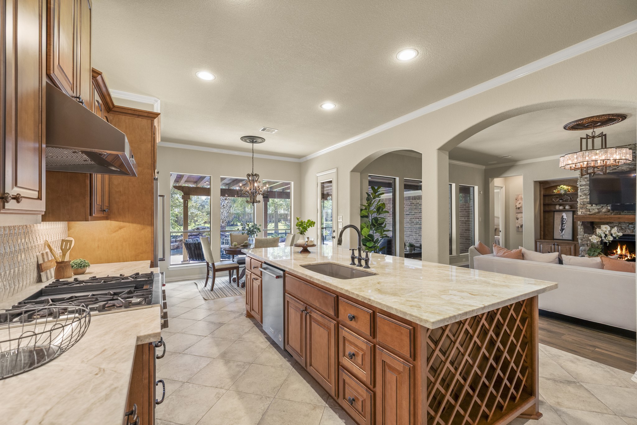 The island draws the space together with Taj Mahal quartzite, rich Benedettini cabinetry, and undercabinet lighting giving the room its custom, elevated feel. The breakfast nook sits ahead near the windows, pulling natural light toward the back of the home, while the arched openings on the right keep the kitchen connected to the living room and the poolside, water-front setting beyond.