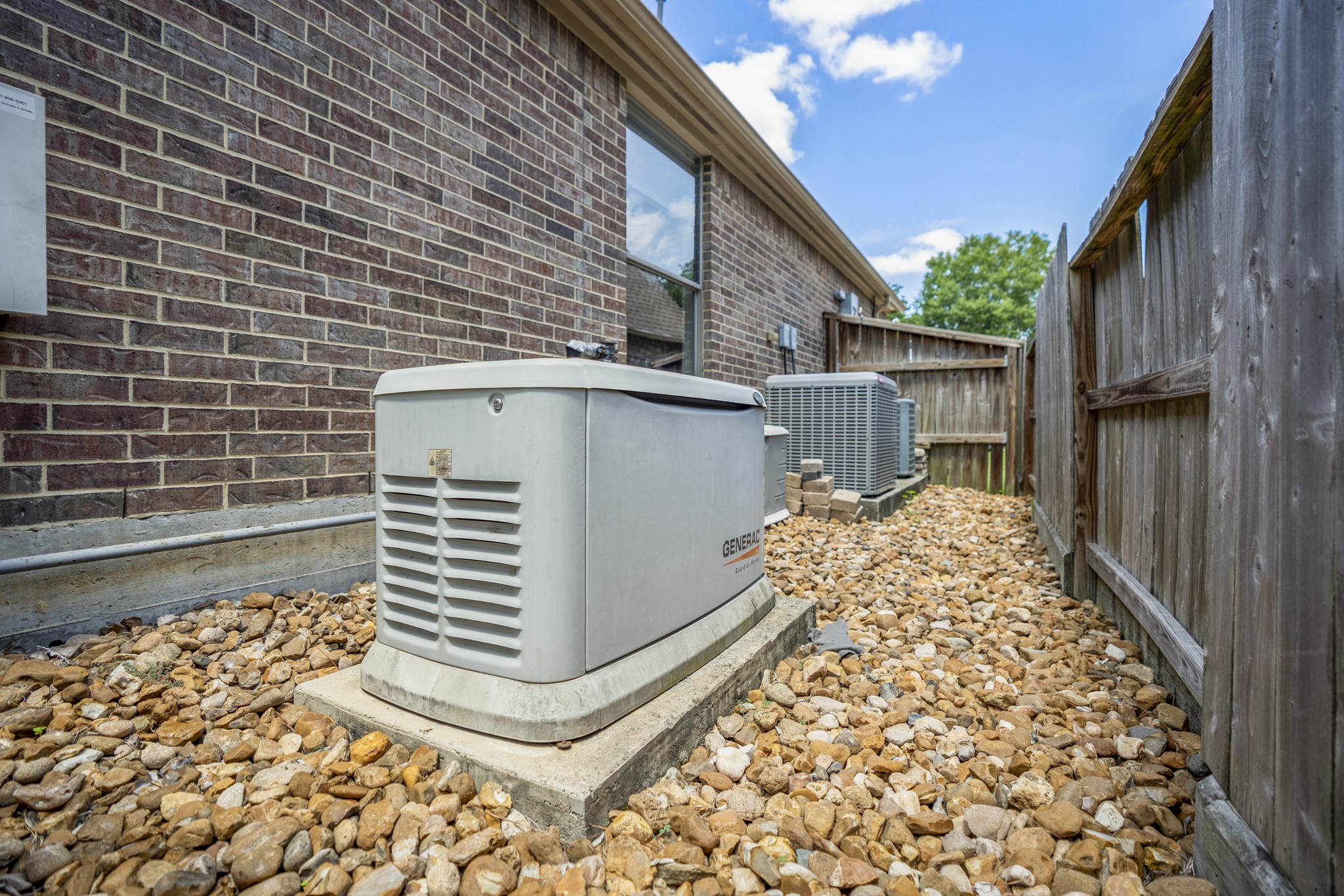 Along the side of the home, the mechanicals are neatly tucked away from the poolside living areas, keeping the backyard experience focused on the water, landscaping, and outdoor space. This view also highlights the practical upgrades buyers care about behind the scenes, including the whole-house Generac generator and A/C equipment positioned with easy exterior access.