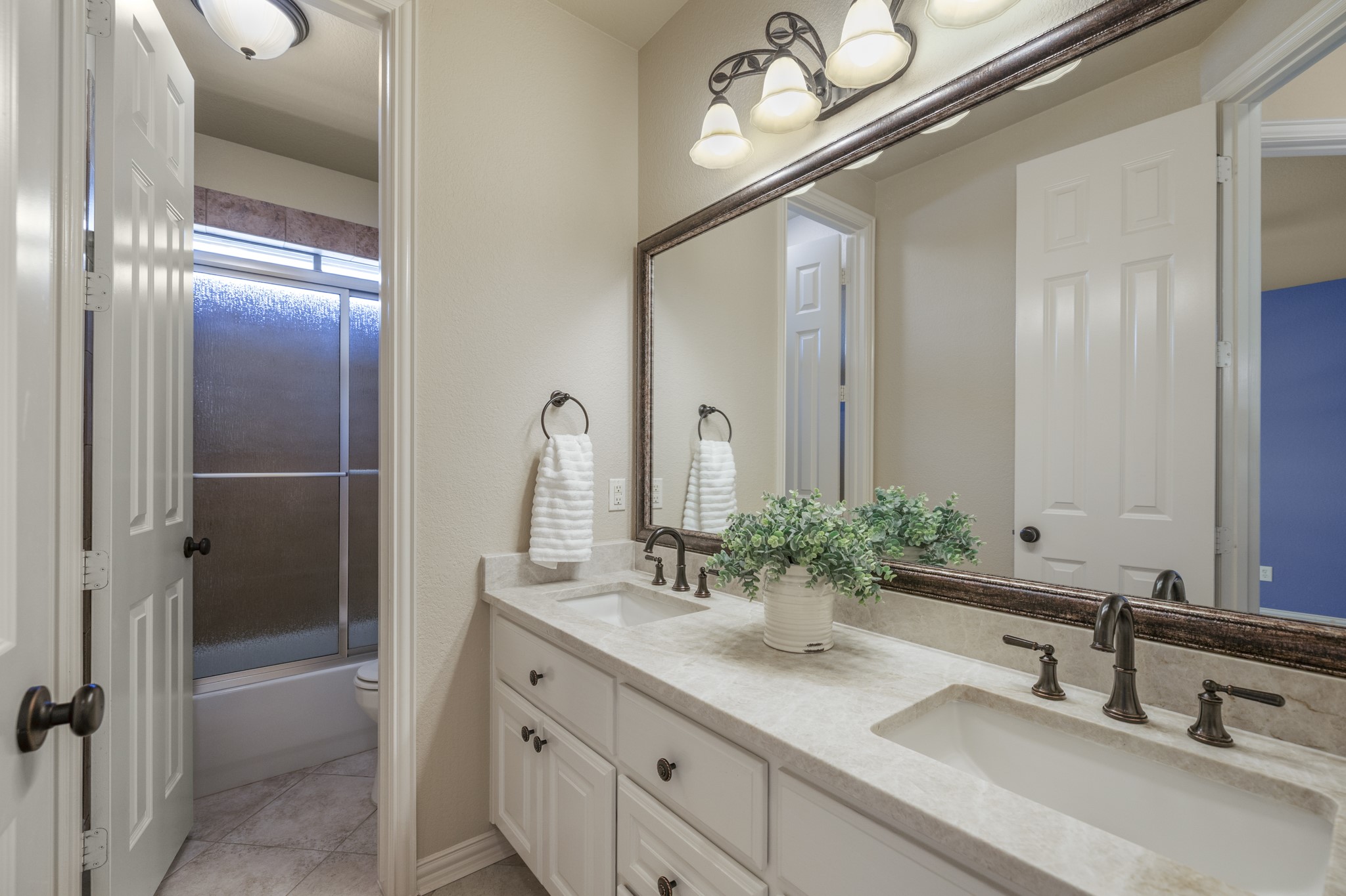 Connected to the second bedroom, this bath continues the suite feel with a double vanity, framed mirrors, upgraded lighting, and a glass-enclosed shower. The doorway on the left leads back into the bedroom, keeping this front-of-home space private and convenient while still feeling polished and connected to the homes custom finishes.