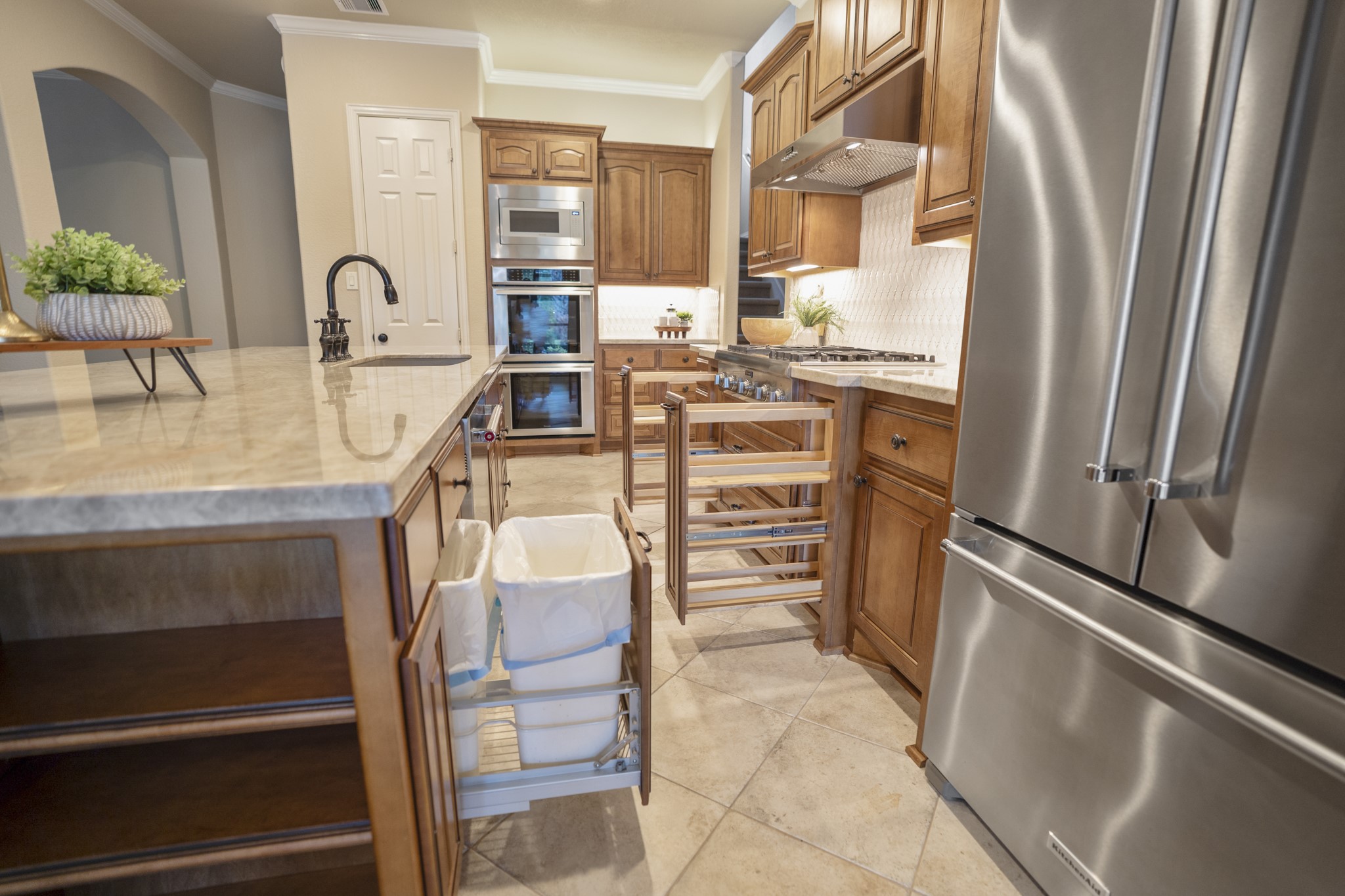 Turning back toward the cooking wall, the kitchen shows how thoughtfully the workspace is arranged with the island and seating to the left, stainless refrigerator to the right, and rich cabinetry wrapping the cooktop and built-in appliance area ahead.