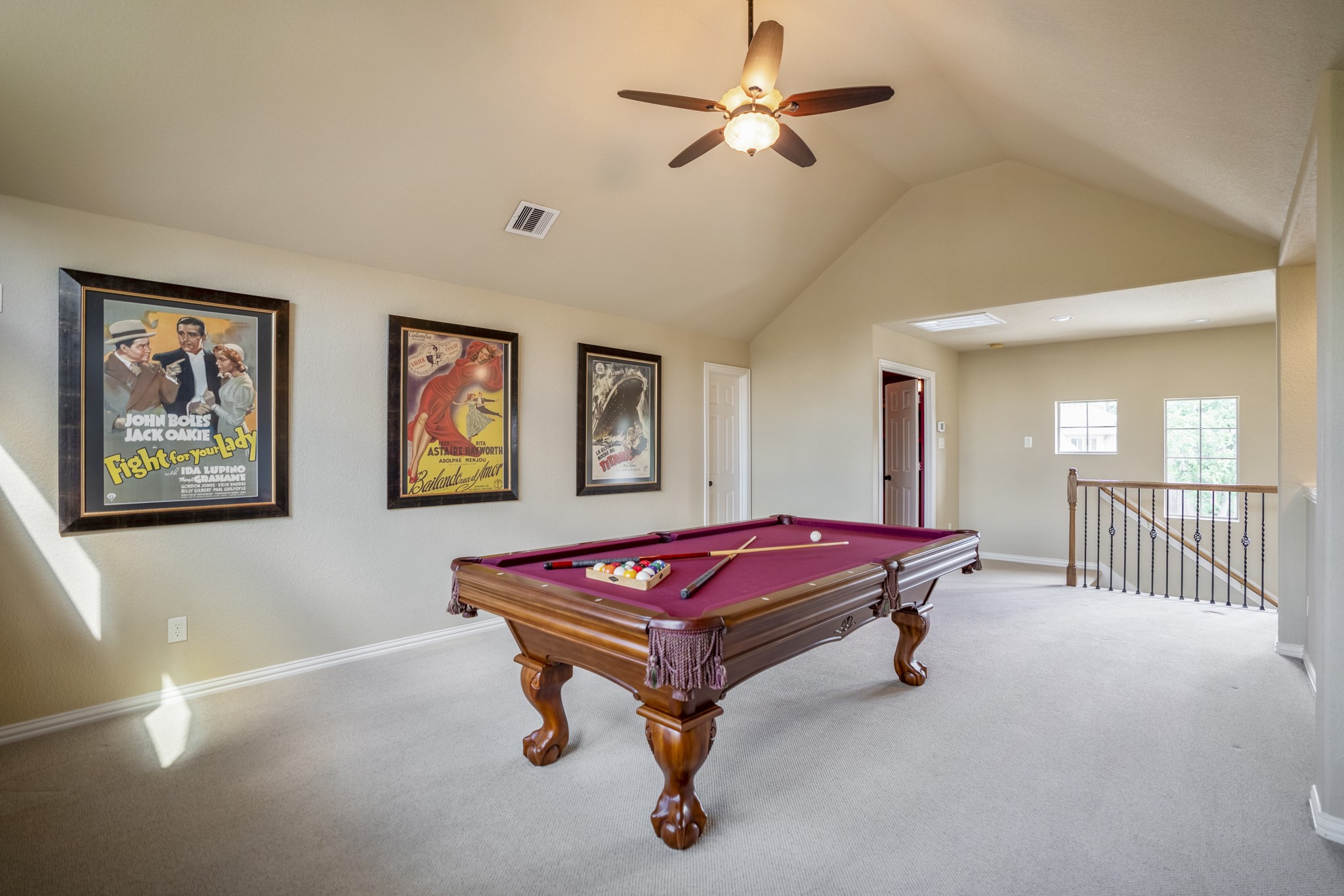 From this angle, the upstairs game room shows how the second level is set up for relaxed entertaining, with the pool table centered in the space and windows bringing in natural light. The door on the left leads to the half bath, while the door across from the stairs opens to the media room, keeping the upstairs layout easy to enjoy for game nights, movies, and time away from the main living areas downstairs.
