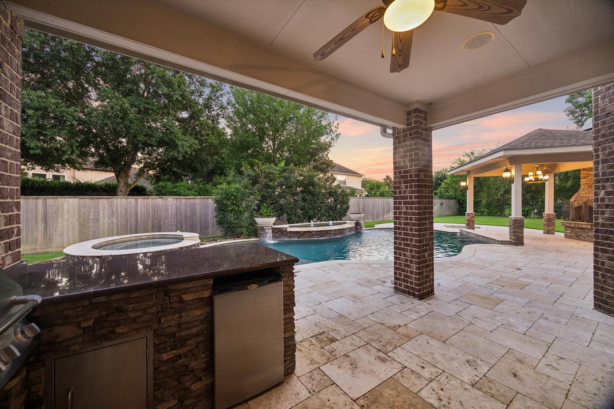 Beautiful outdoor living space featuring a covered outdoor kitchen, travertine flooring, resort-style pool and spa, and generous entertaining areas. Designed for memorable gatherings with family and friends, this backyard oasis is ready to be enjoyed all summer long and beyond.