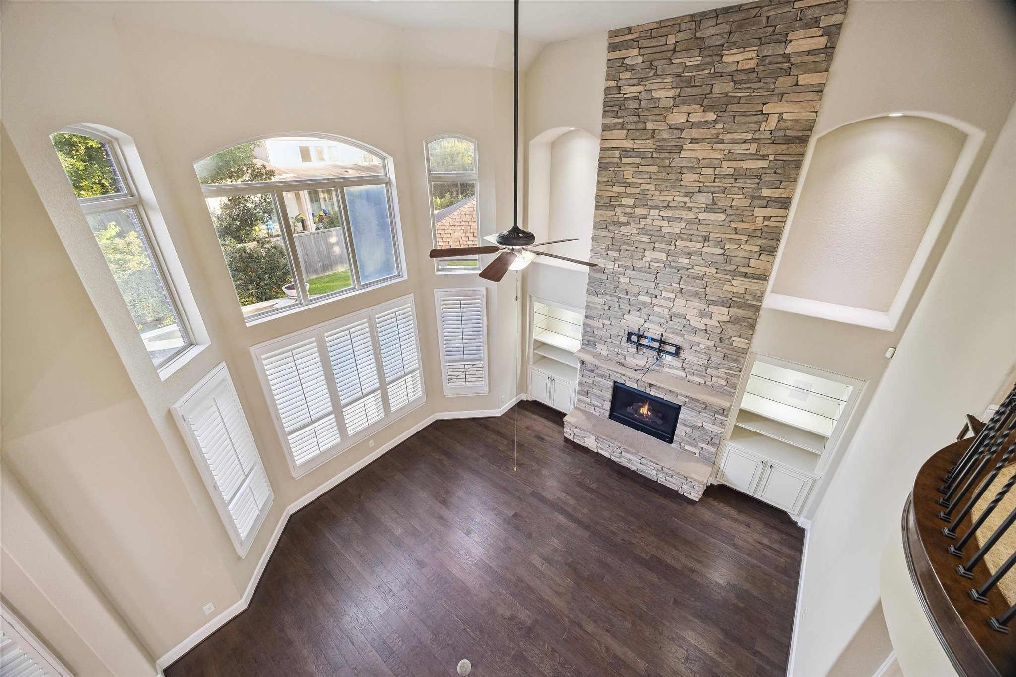 A breathtaking perspective from the upper-level iron-railed balcony reveals the grandeur of the family room, where soaring ceilings, a striking floor-to-ceiling stone fireplace, and expansive windows create a bright and inviting atmosphere.