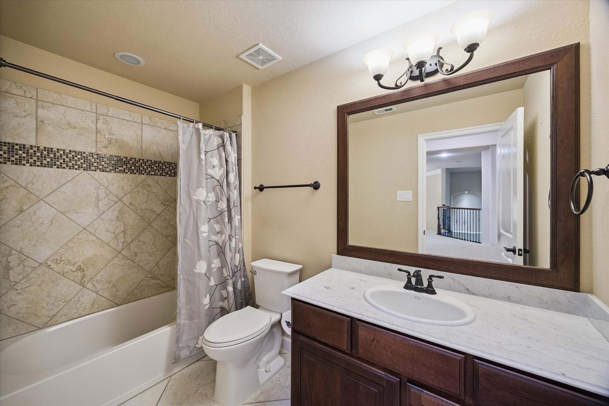 A well-appointed secondary bathroom conveniently located off the upstairs landing. Featuring a spacious vanity with marble-look countertops, elegant framed mirror, and a tub/shower combination accented with decorative tile work, this bathroom comfortably serves family members and guests alike.