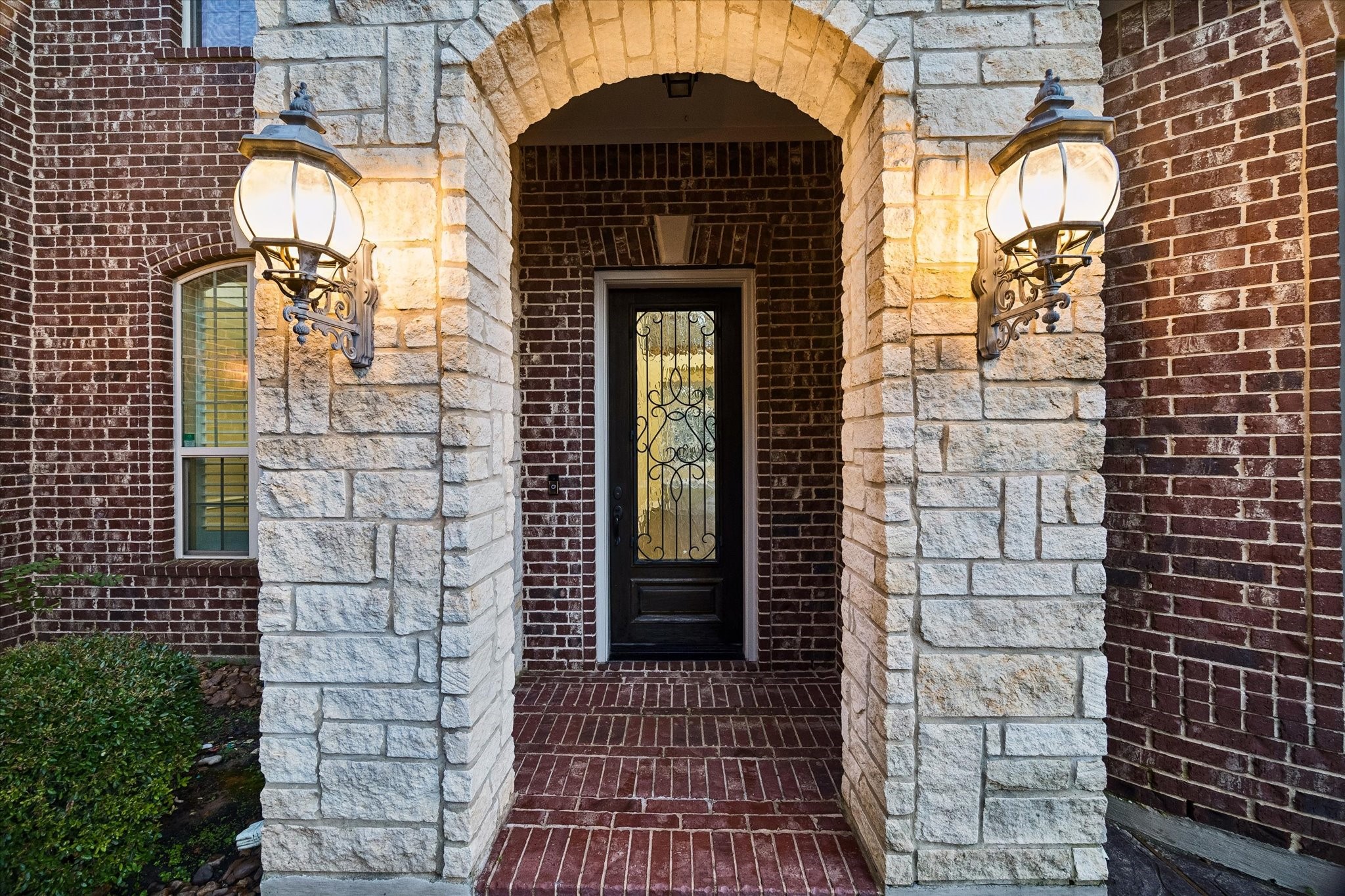 The elegant entry welcomes guests with timeless architectural details, including a custom iron-and-glass front door, warm lantern-style lighting, and a beautiful combination of rich brick and natural stone finishes. The elegant entry welcomes guests with timeless architectural details, including a custom iron-and-glass front door, warm lantern-style lighting, and a beautiful combination of rich brick and natural stone finishes.