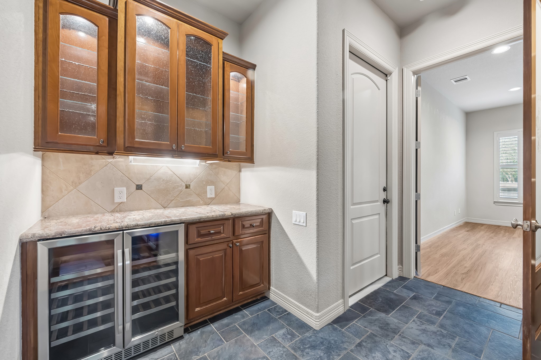 Elegant butler's pantry with rich wood cabinetry, glass display doors, and a wine fridge.