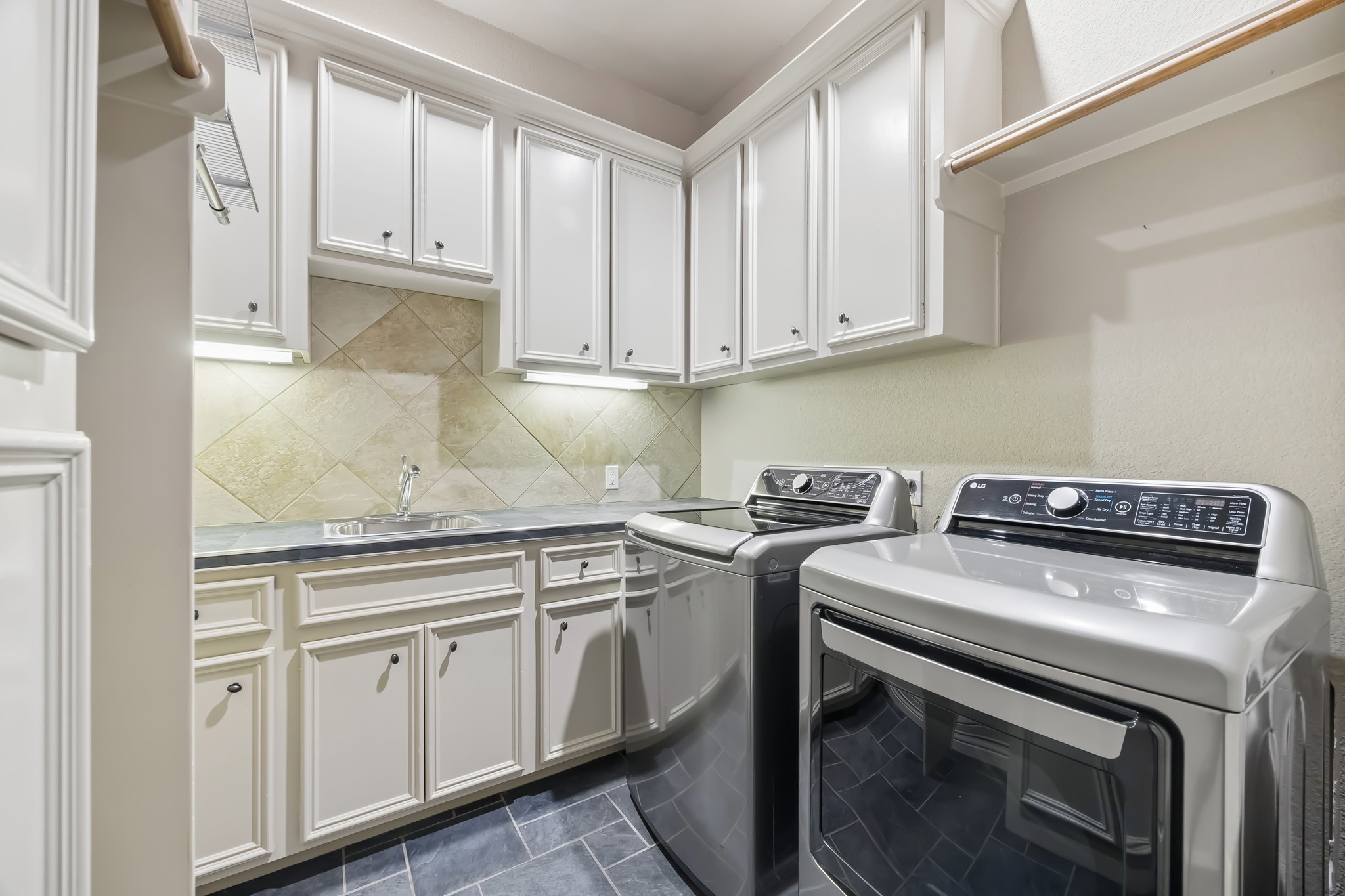 Modern laundry room featuring sleek appliances, ample cabinetry for storage, and a convenient utility sink.