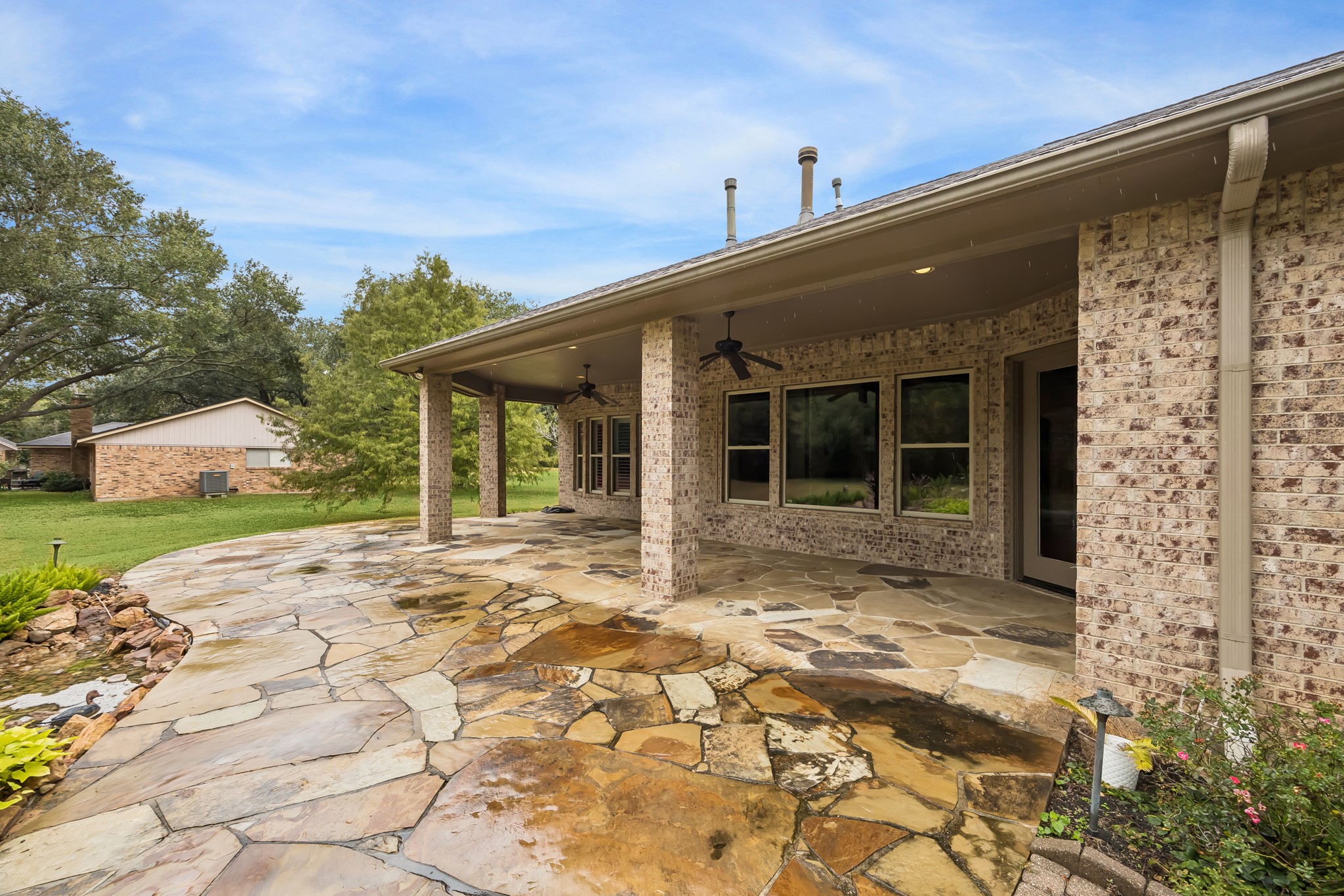 Expansive stone patio with covered seating area, surrounded by lush greenery, perfect for outdoor relaxation and entertaining.