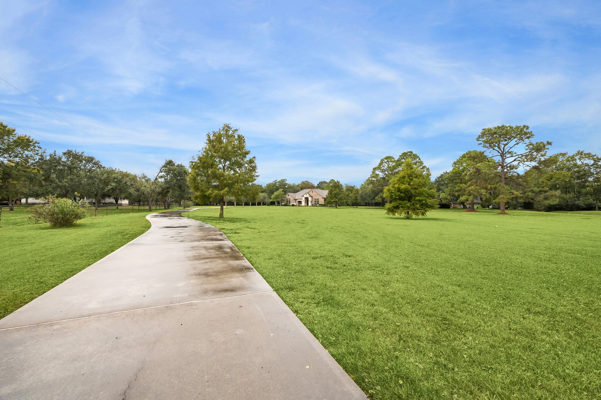 Expansive green lawn with a long, winding driveway leading to the home surrounded by mature trees.