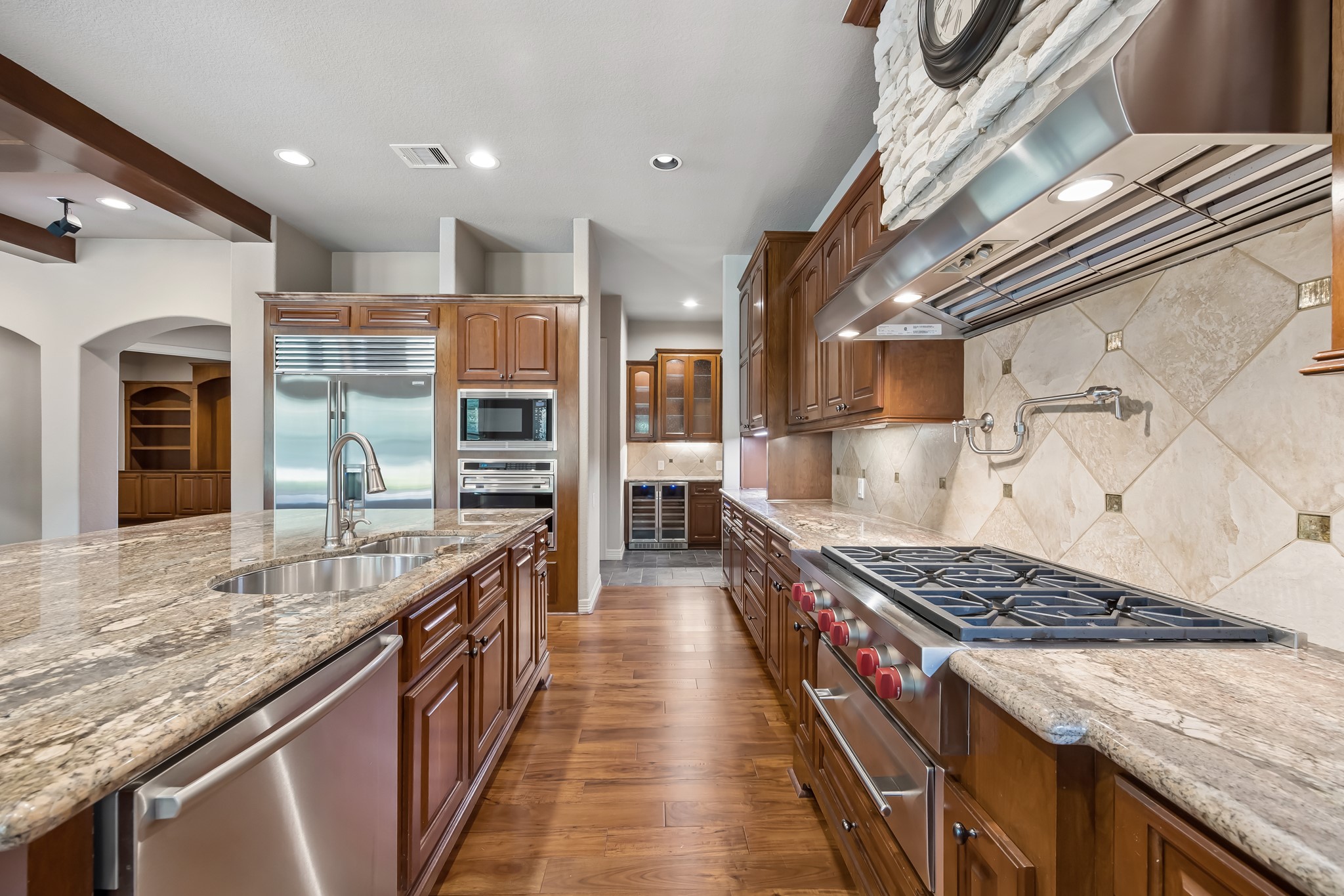 Spacious gourmet kitchen featuring elegant granite countertops, high-end stainless steel appliances, wine refrigerator and rich wooden cabinetry, perfect for culinary enthusiasts.