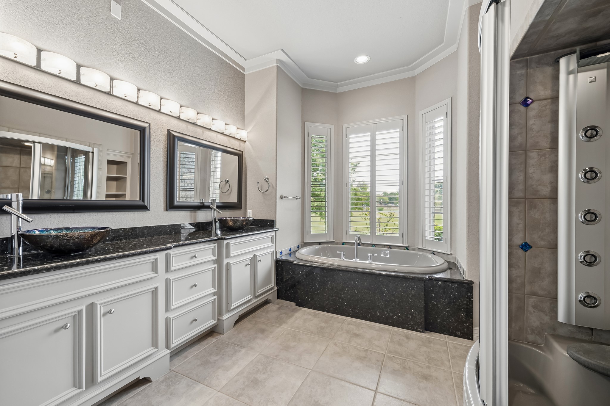 Luxurious bathroom featuring a sleek double vanity with vessel sinks, a relaxing corner jetted tub framed by bright windows, and a modern shower with multiple jets.