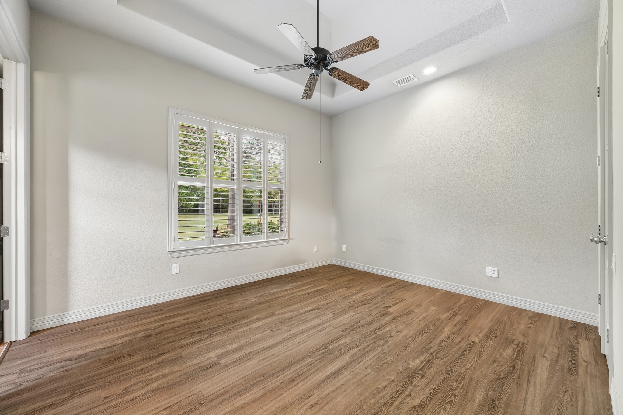 Bright and spacious room featuring elegant wood flooring, a stylish ceiling fan, and large windows with plantation shutters that offer a serene view of the outdoors. Guest Bedroom