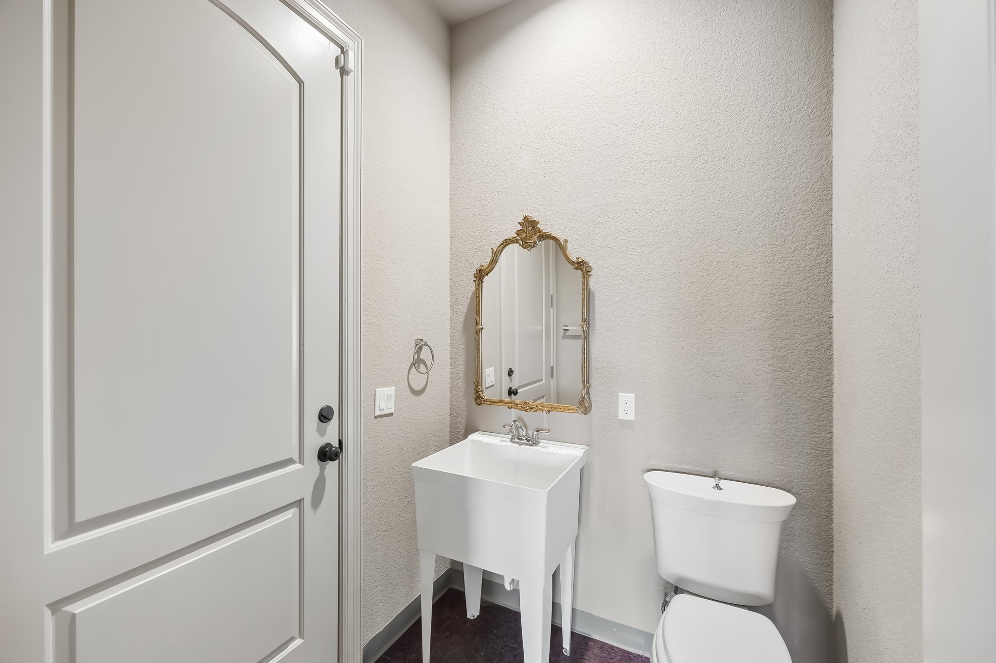 Half-bathroom featuring a classic pedestal sink with a gold-framed mirror and modern fixtures, set against soft, neutral walls.  Door exits to the garage.
