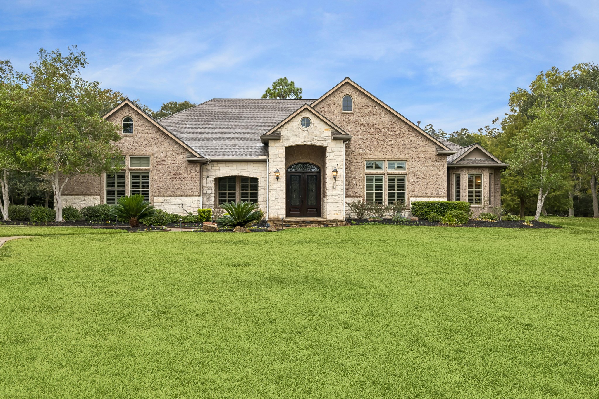 Charming brick home with elegant arched entry, surrounded by lush greenery and mature trees, offering serene suburban living.