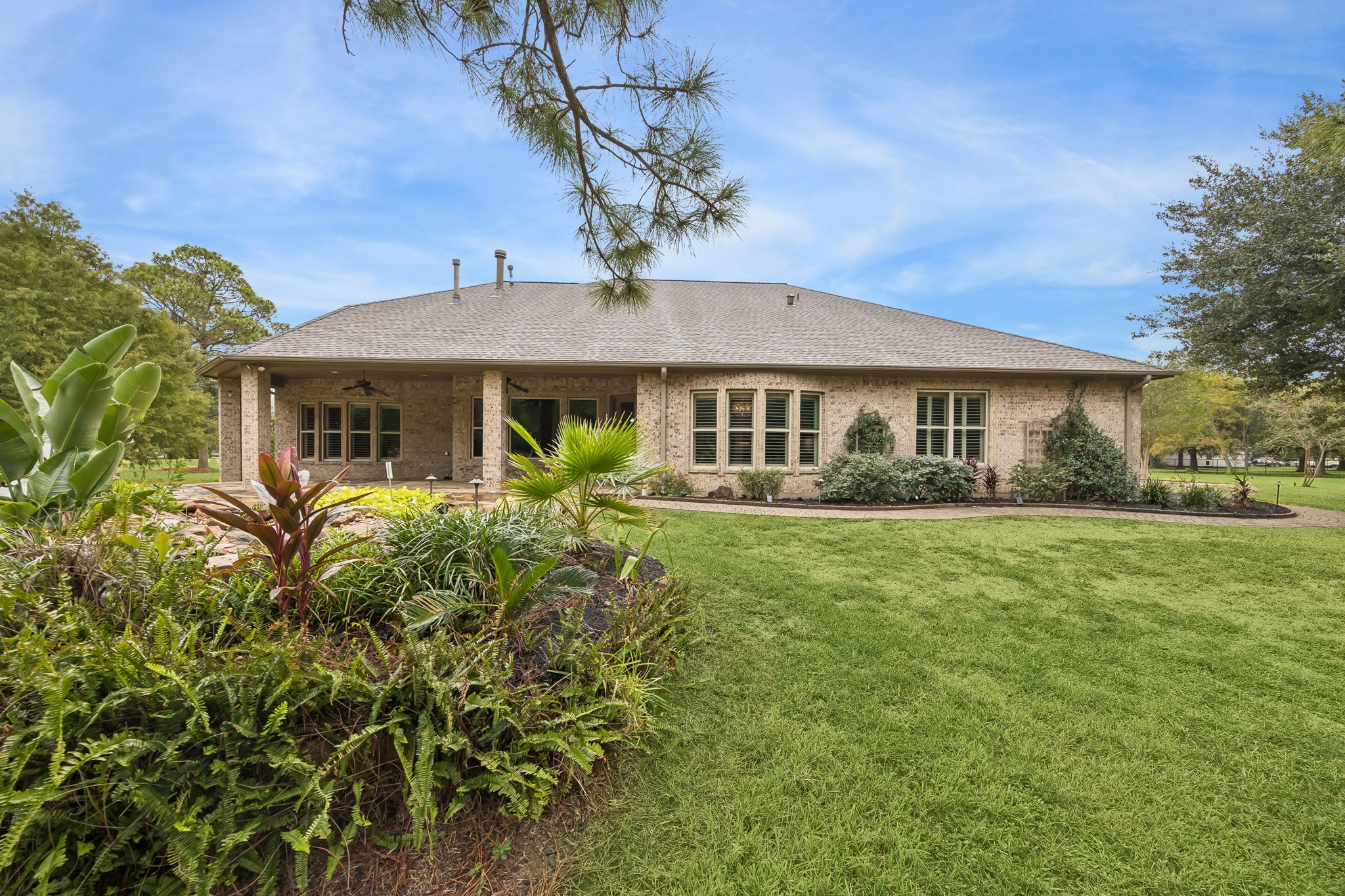 Expansive brick home with a charming covered patio, surrounded by lush landscaping and a well-maintained lawn, perfect for outdoor enjoyment.