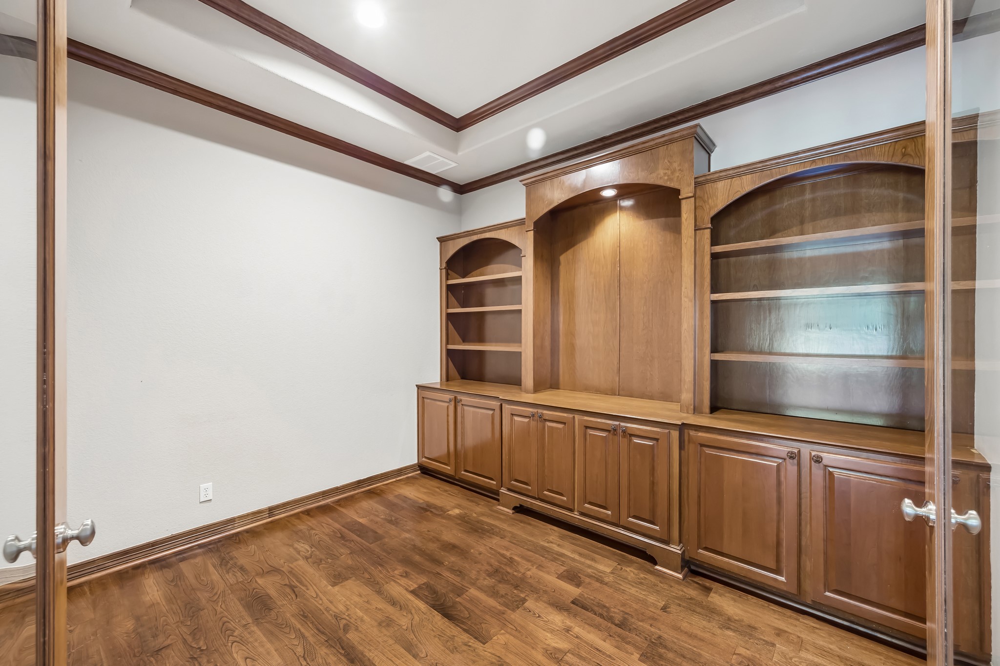 Elegant study with rich wood flooring and custom built-in shelving, perfect for a home library or office.