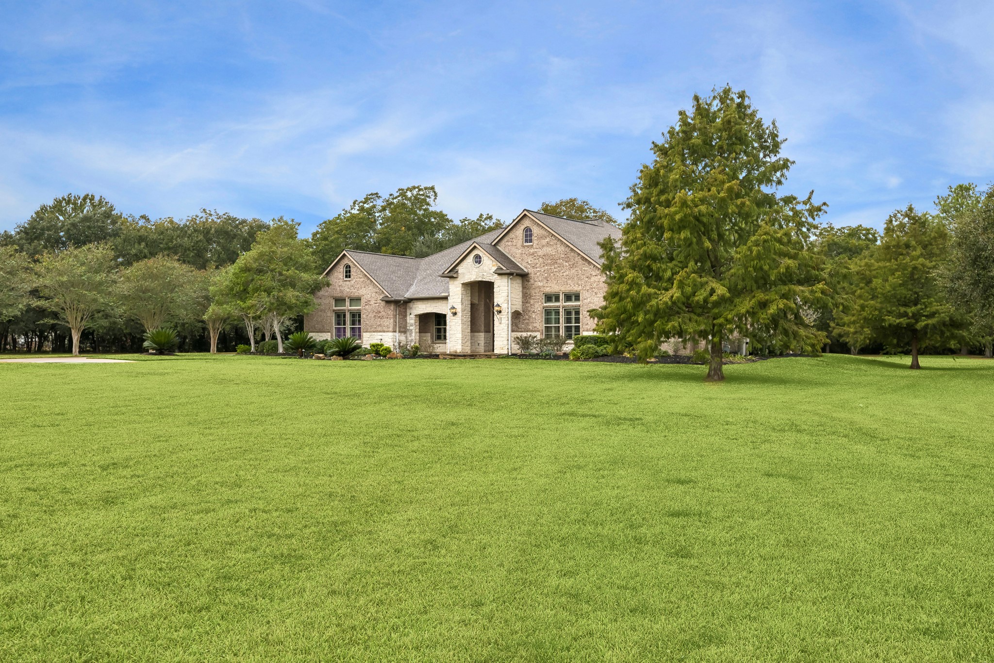Charming brick home nestled on a sprawling, lush green lawn with mature trees, offering serene privacy and a picturesque setting.