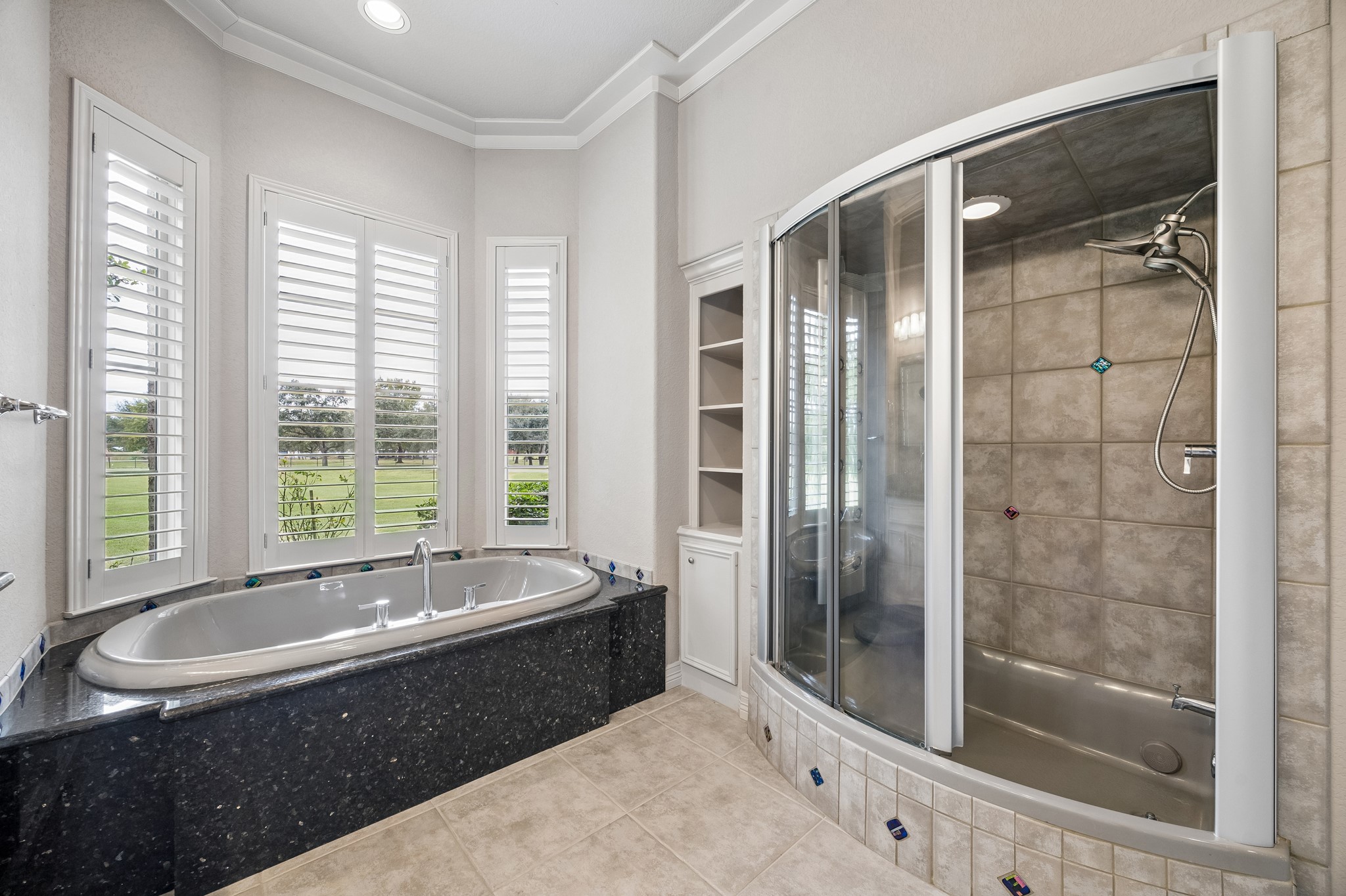 Luxurious bathroom with a large soaking tub, elegant tile shower, and abundant natural light from stylish plantation shutters.