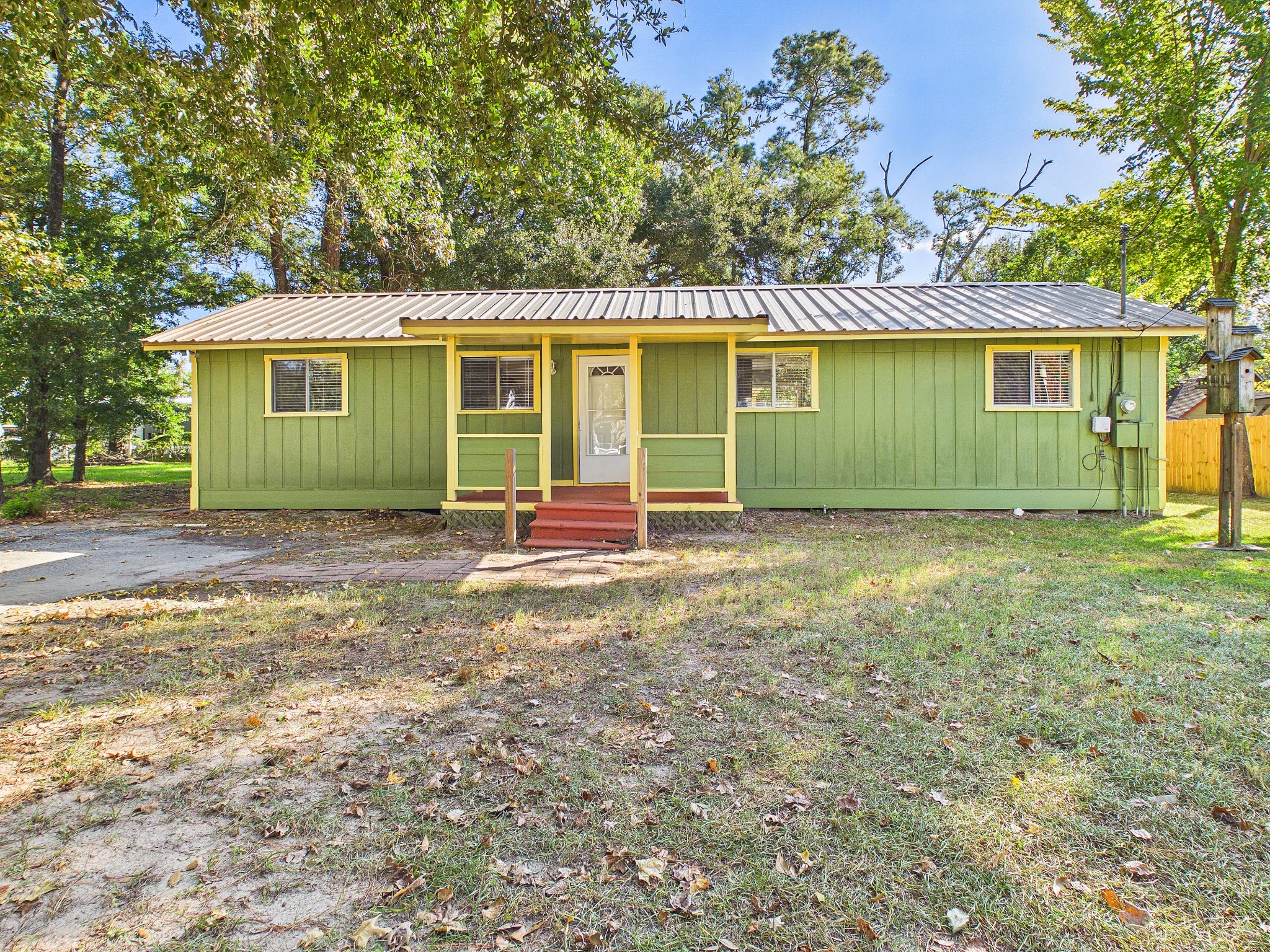 Charming single-story home with a bright green facade, metal roof, and cozy front porch, surrounded by mature trees in a serene setting.