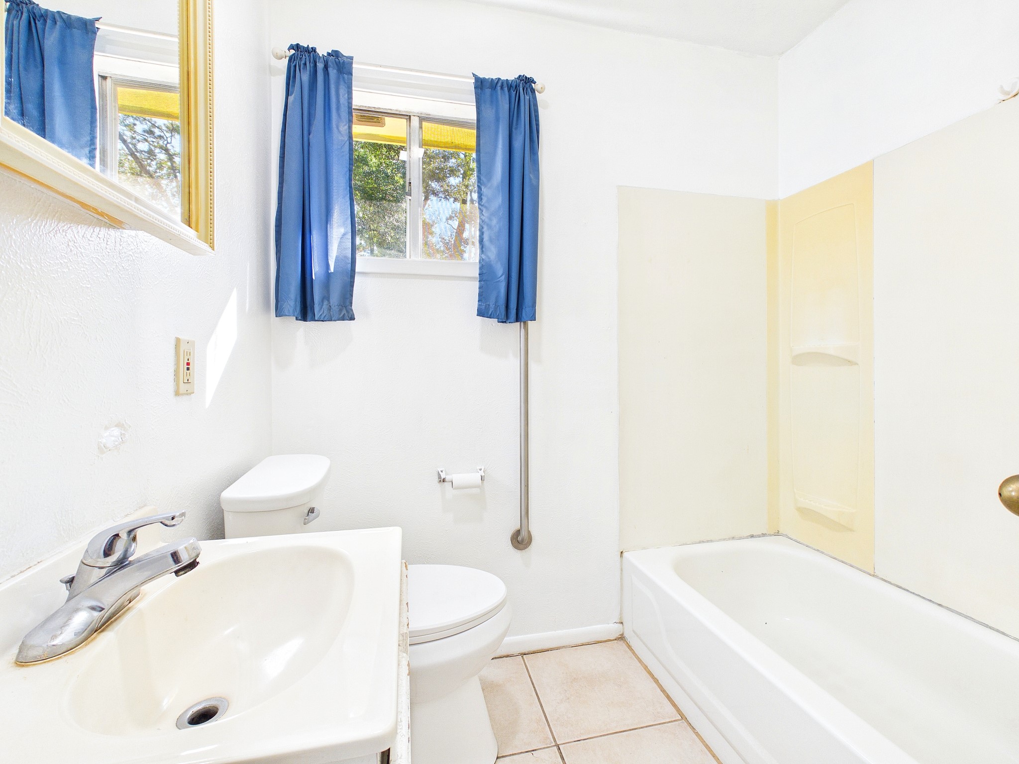 Bright bathroom featuring a clean white sink, bathtub, and toilet, complemented by blue curtains and a convenient window for natural light.