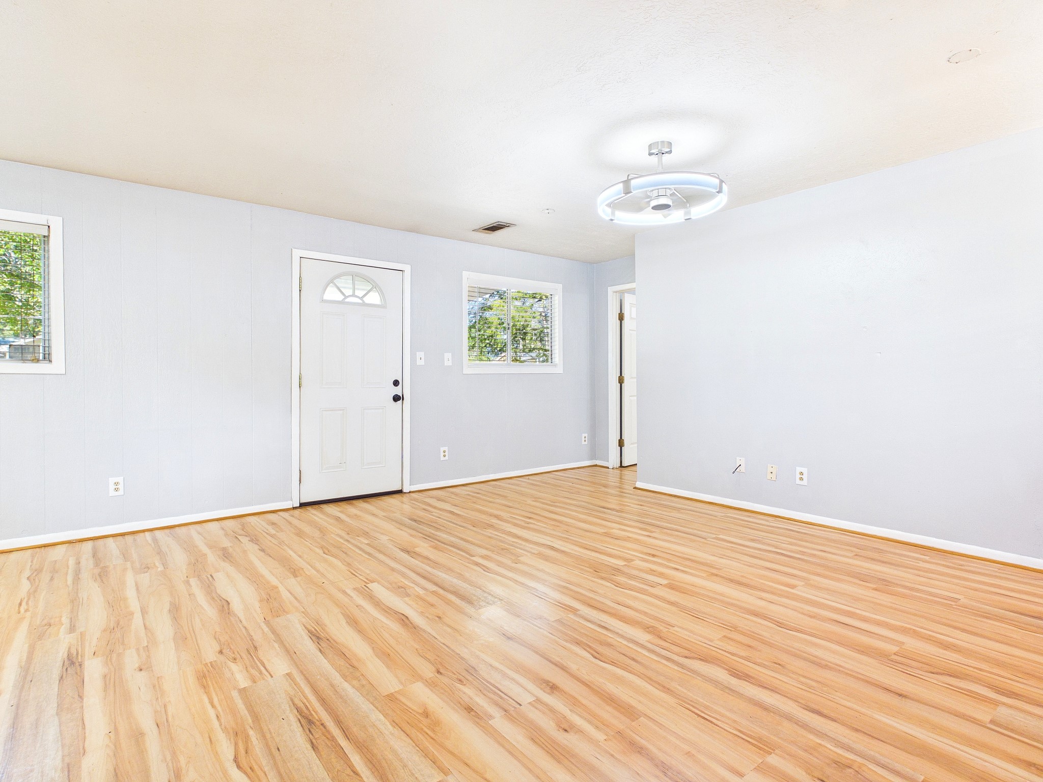 Bright and inviting living space with sleek wood-look floors, modern light fixtures, and ample natural light from large windows.