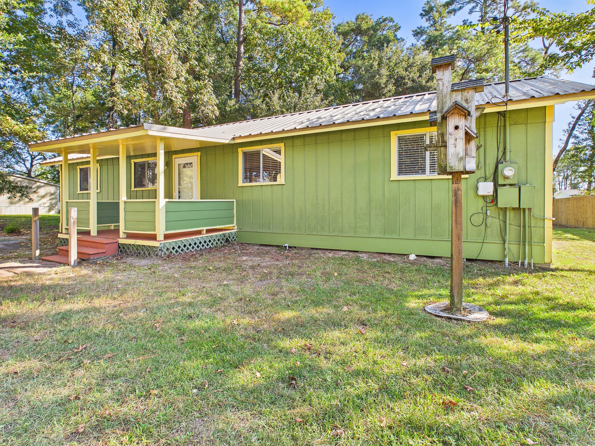 Charming green cottage with a welcoming front porch, nestled in a serene, wooded setting.
