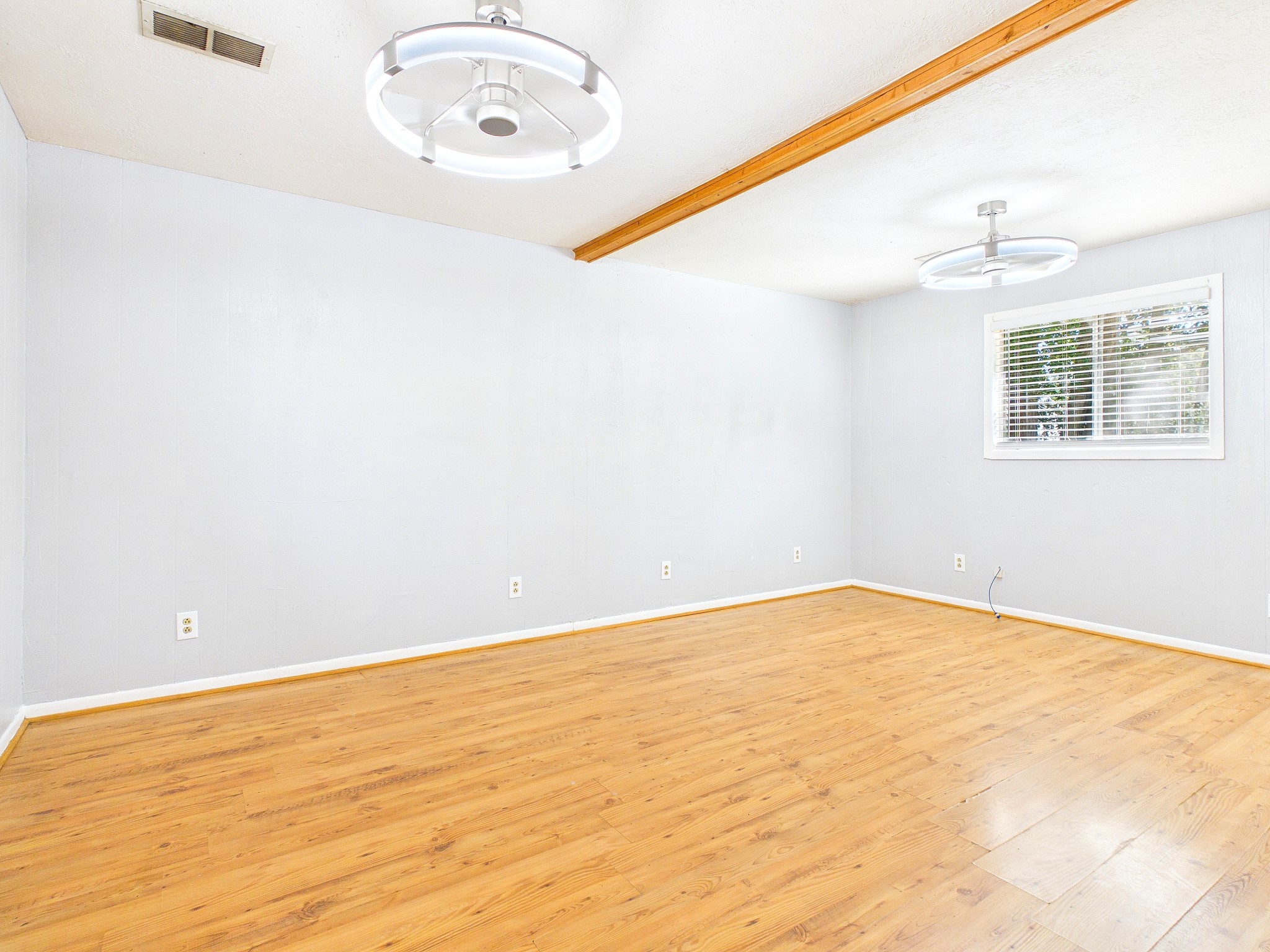 Bright and spacious room featuring sleek floors, modern light fixtures, and a large window that invites ample natural light.