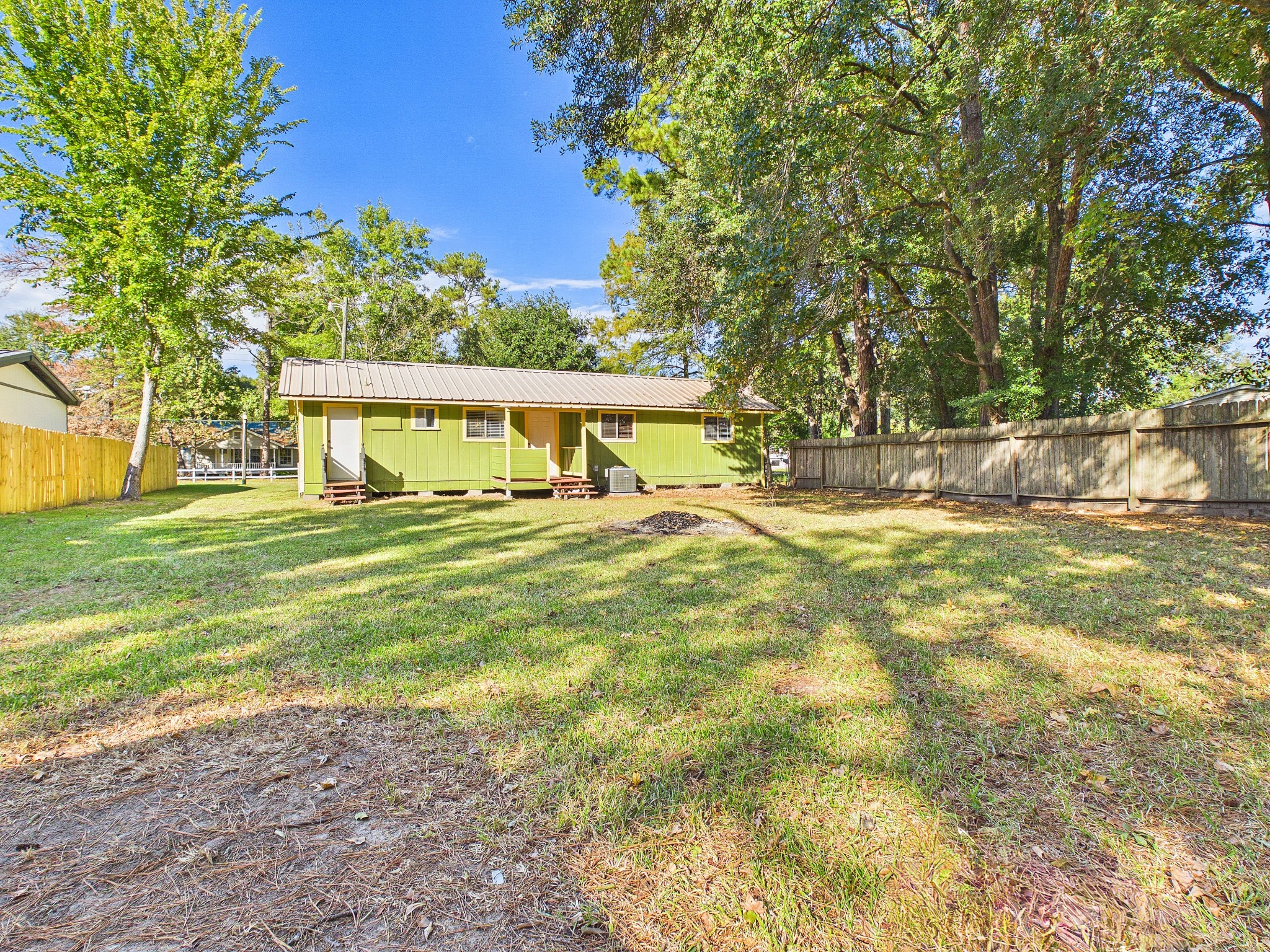 Expansive backyard with lush greenery and mature trees, perfect for outdoor activities, featuring a charming green house with a welcoming porch.