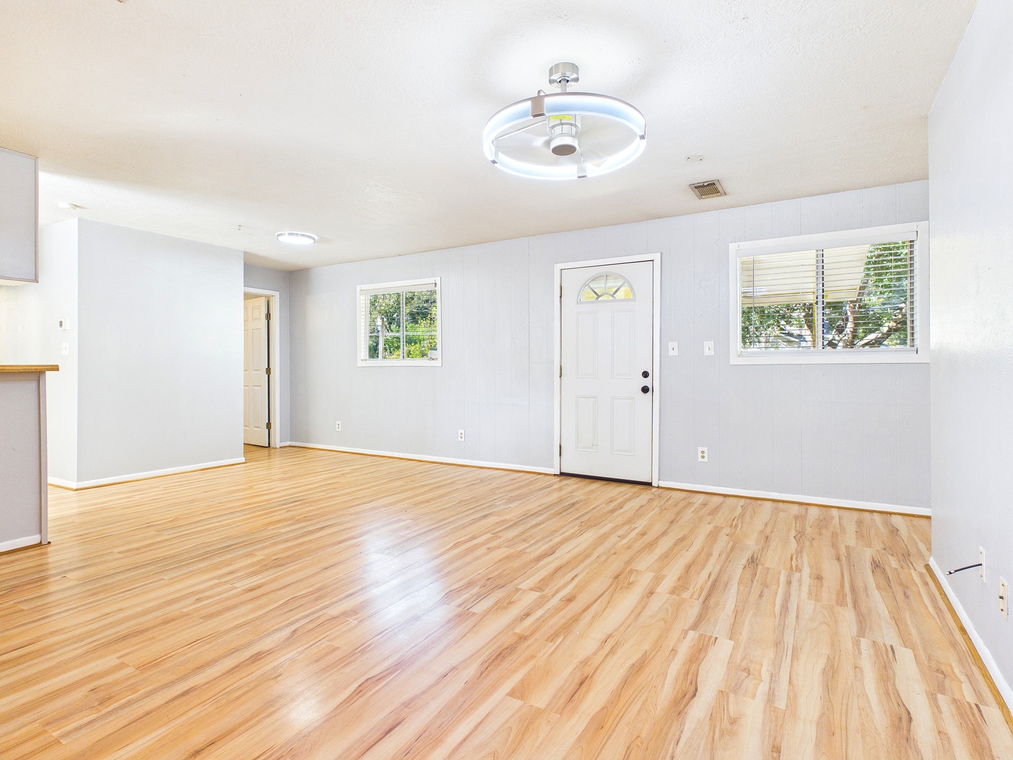Bright and spacious living area featuring sleek wood-look floors, modern lighting, and ample natural light from large windows, perfect for comfortable living and entertaining.