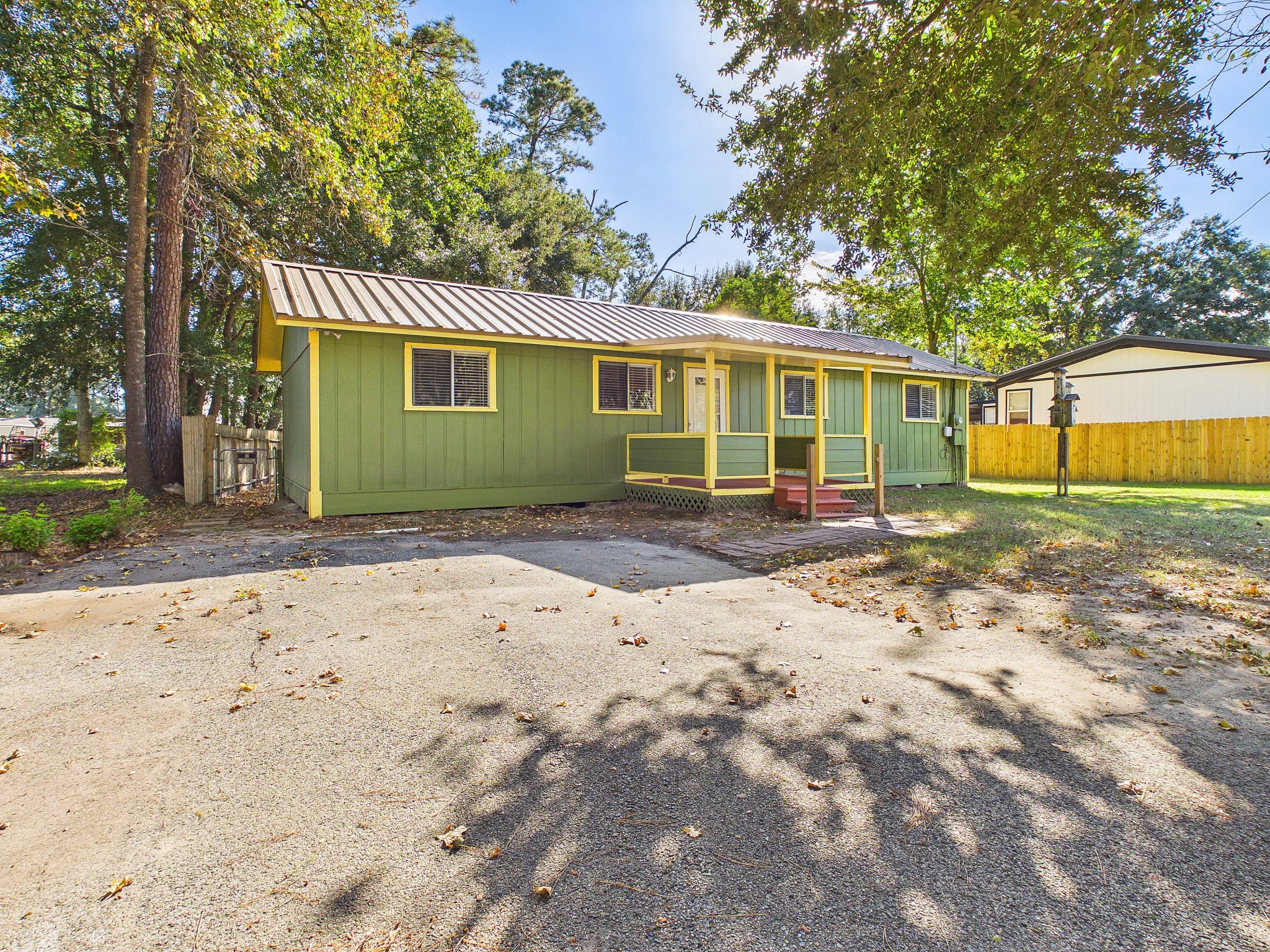 Charming single-story home with a welcoming front porch, nestled among mature trees, featuring a vibrant exterior and a spacious driveway.