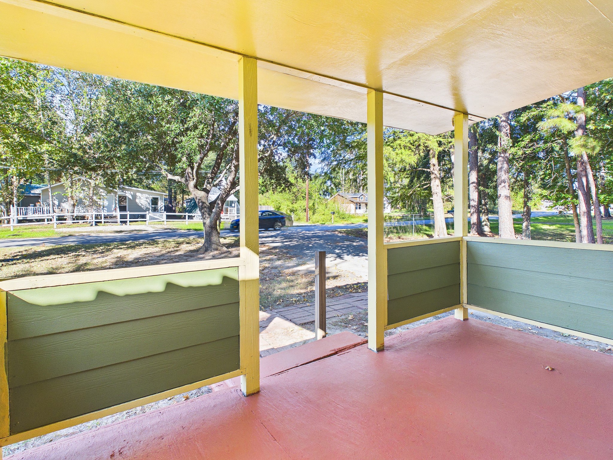 Charming front porch with colorful details offers a serene view of lush trees and a quiet neighborhood street.
