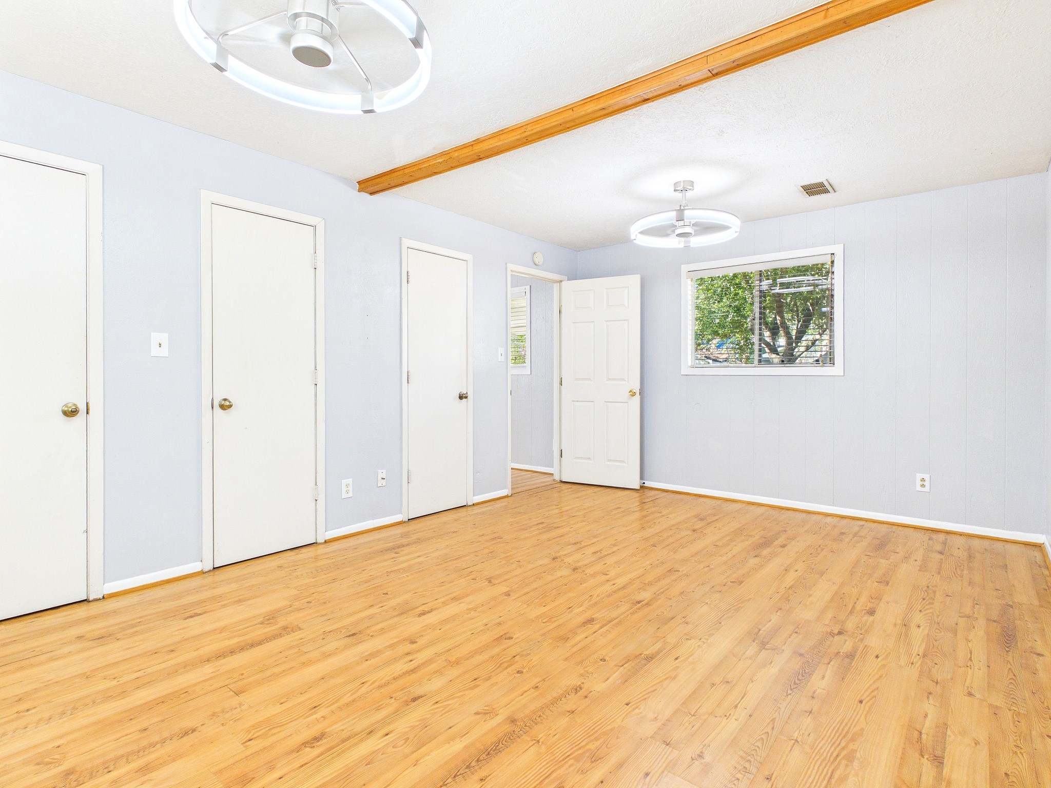Spacious and bright room featuring sleek flooring, modern light fixtures, and ample storage with multiple doors, creating a versatile living space.