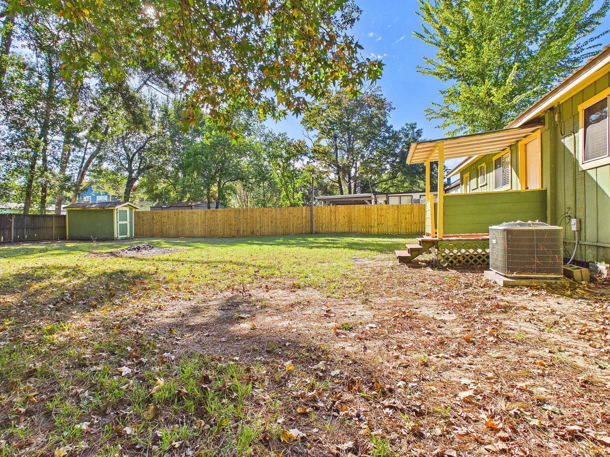Spacious backyard with mature trees, a storage shed, and a charming covered porch, perfect for outdoor relaxation and activities.