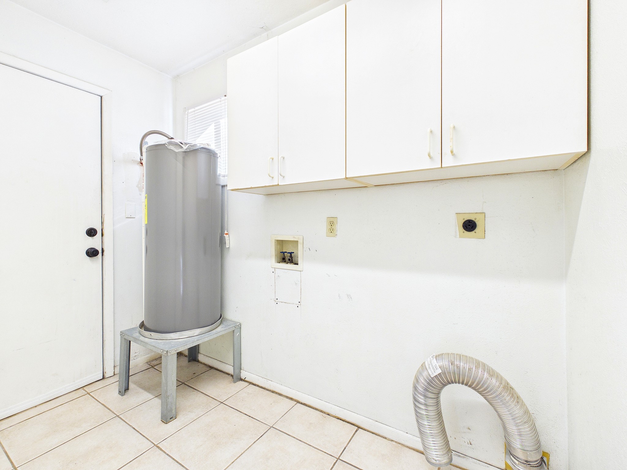 Utility room equipped with a modern water heater, ample storage cabinets, and connections for laundry appliances, all set on durable tiled flooring.