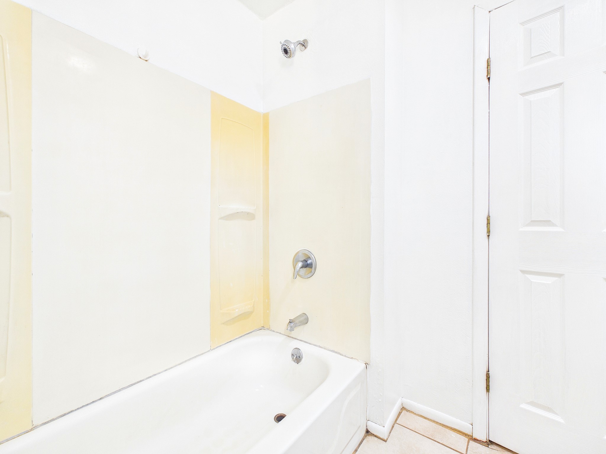 Bright bathroom featuring a classic white tub with a shower, complemented by neutral tile accents and a clean, minimalistic design.