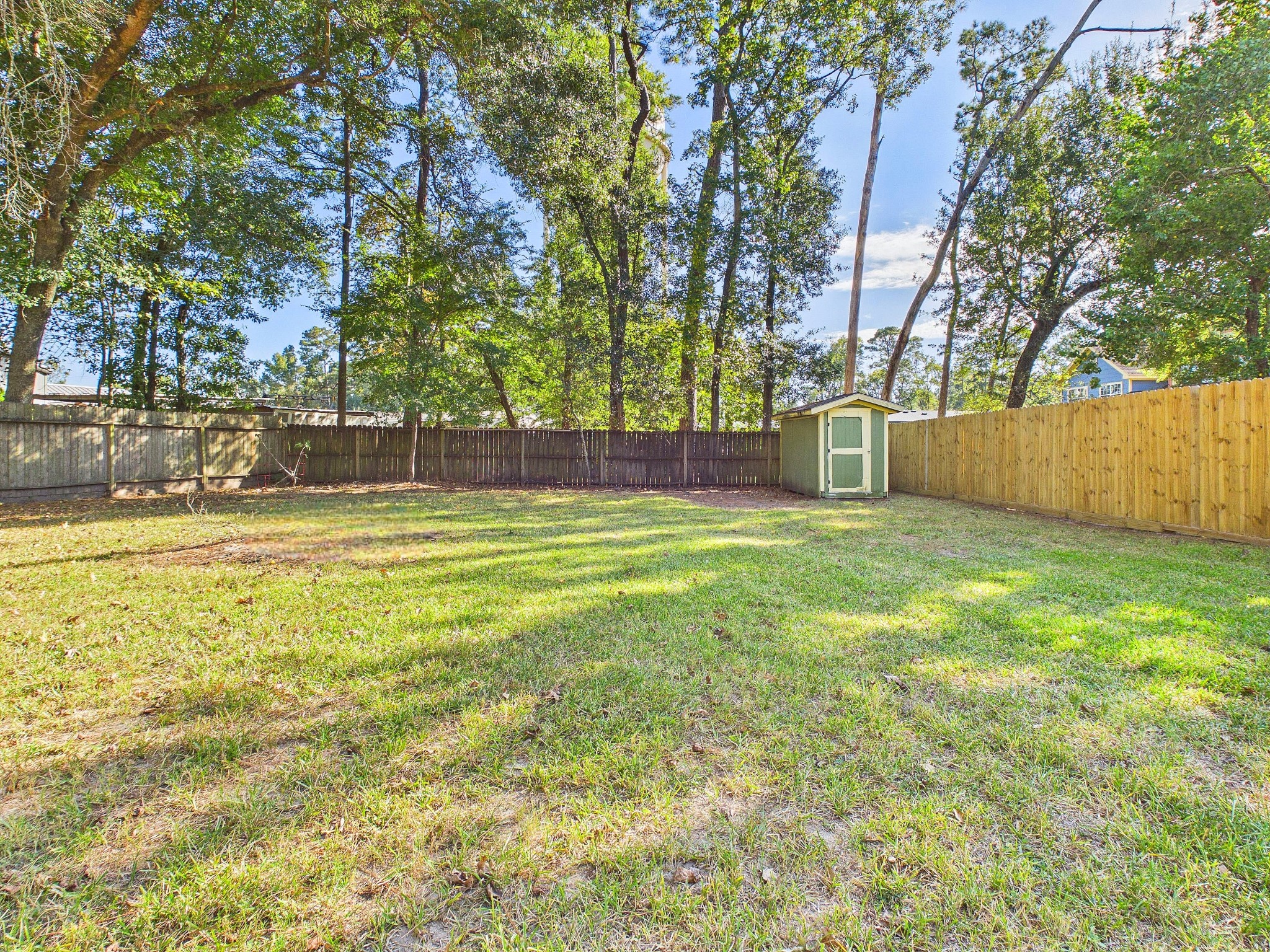Expansive backyard with lush greenery, surrounded by a privacy fence, featuring a charming storage shed.