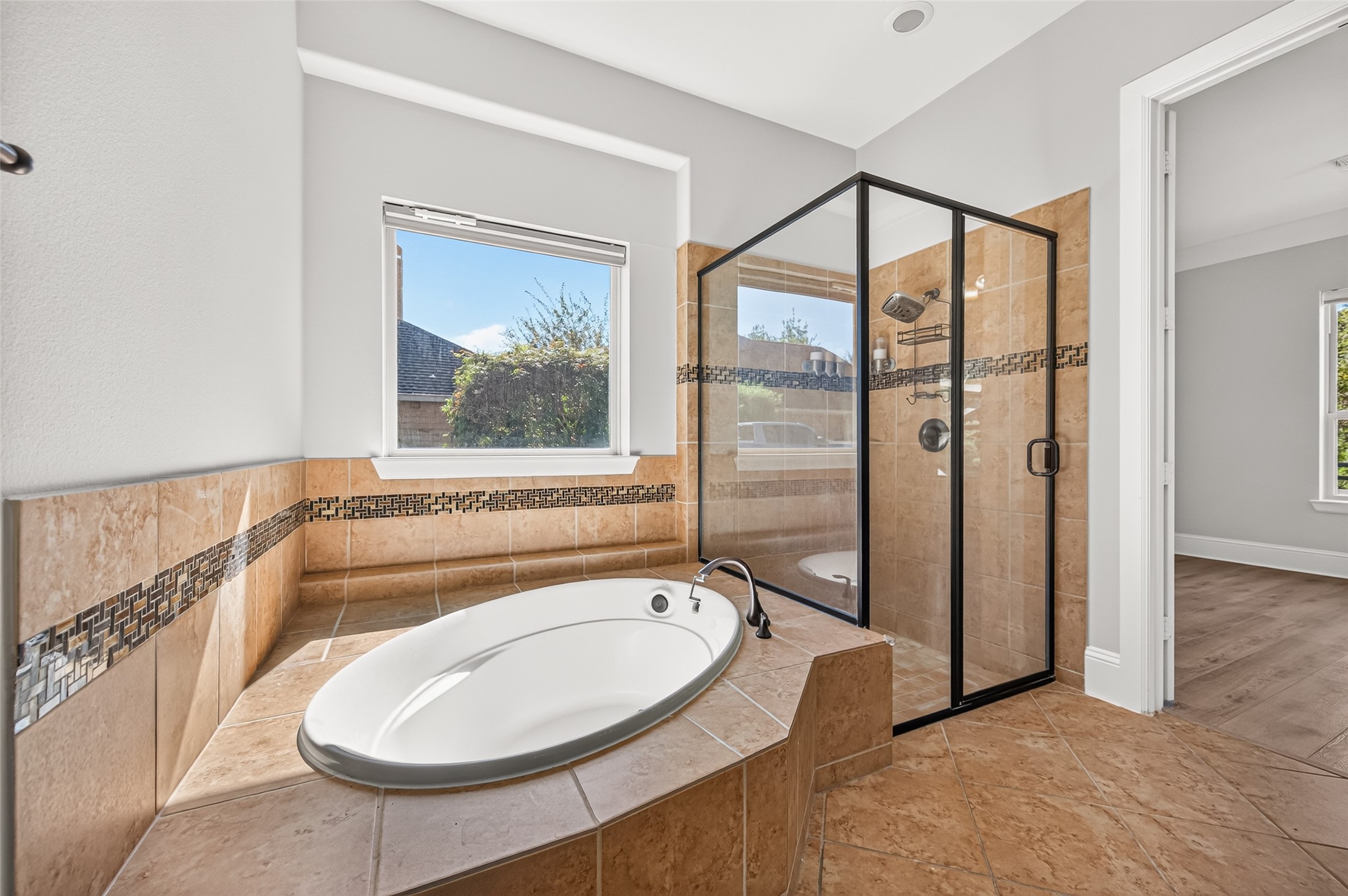 Spa-like primary bath! Indulge in the deep corner soaking tub with elegant tile detailing. Features a massive granite-topped vanity with dual sinks, rich wood cabinetry, a large framed mirror, stylish lighting, and a massive walk-in layout.