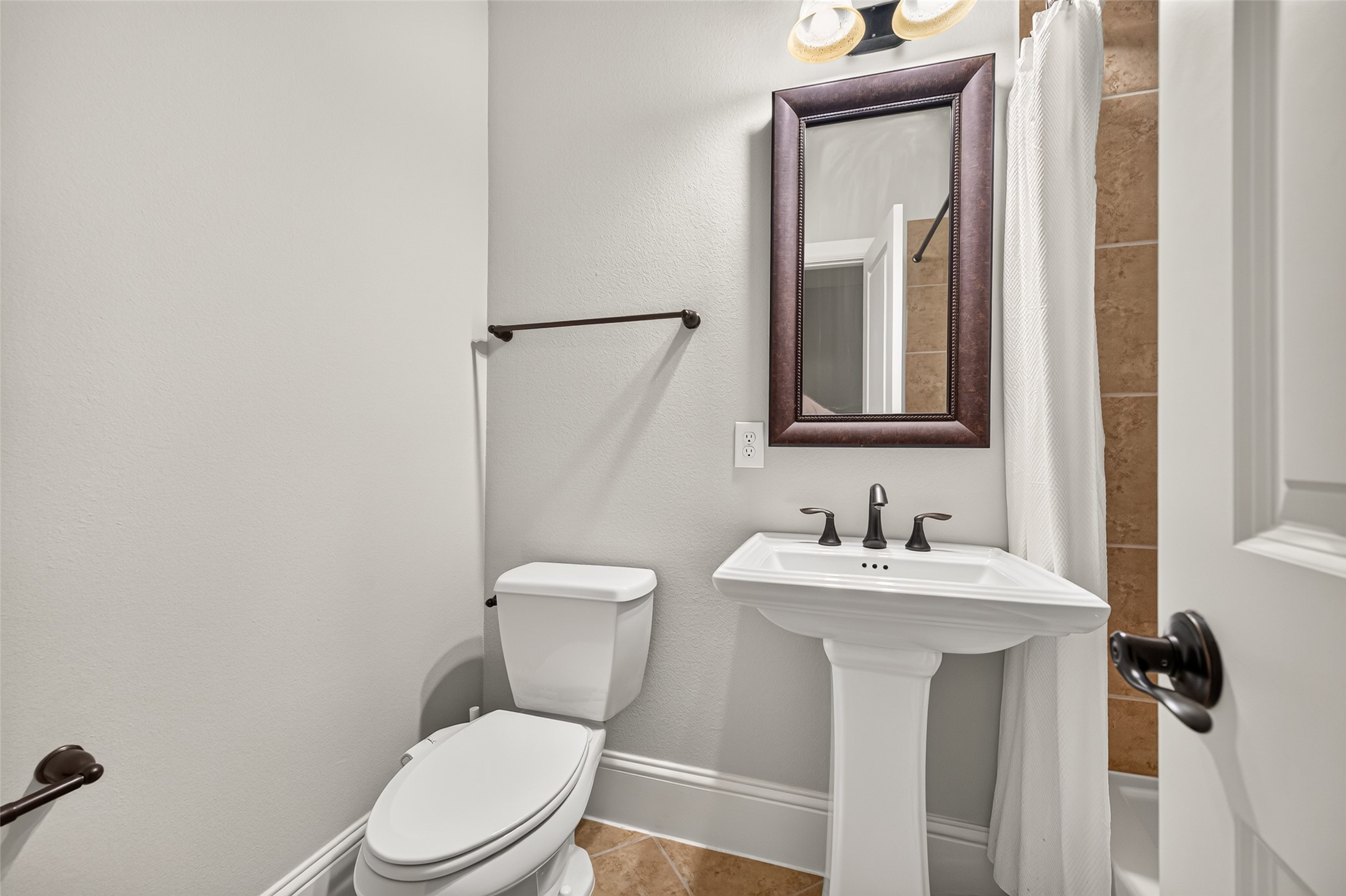 Conveniently located powder room perfect for guests! Features a classic porcelain pedestal sink, elegant oil-rubbed bronze fixtures, a framed mirror, and durable tile flooring.