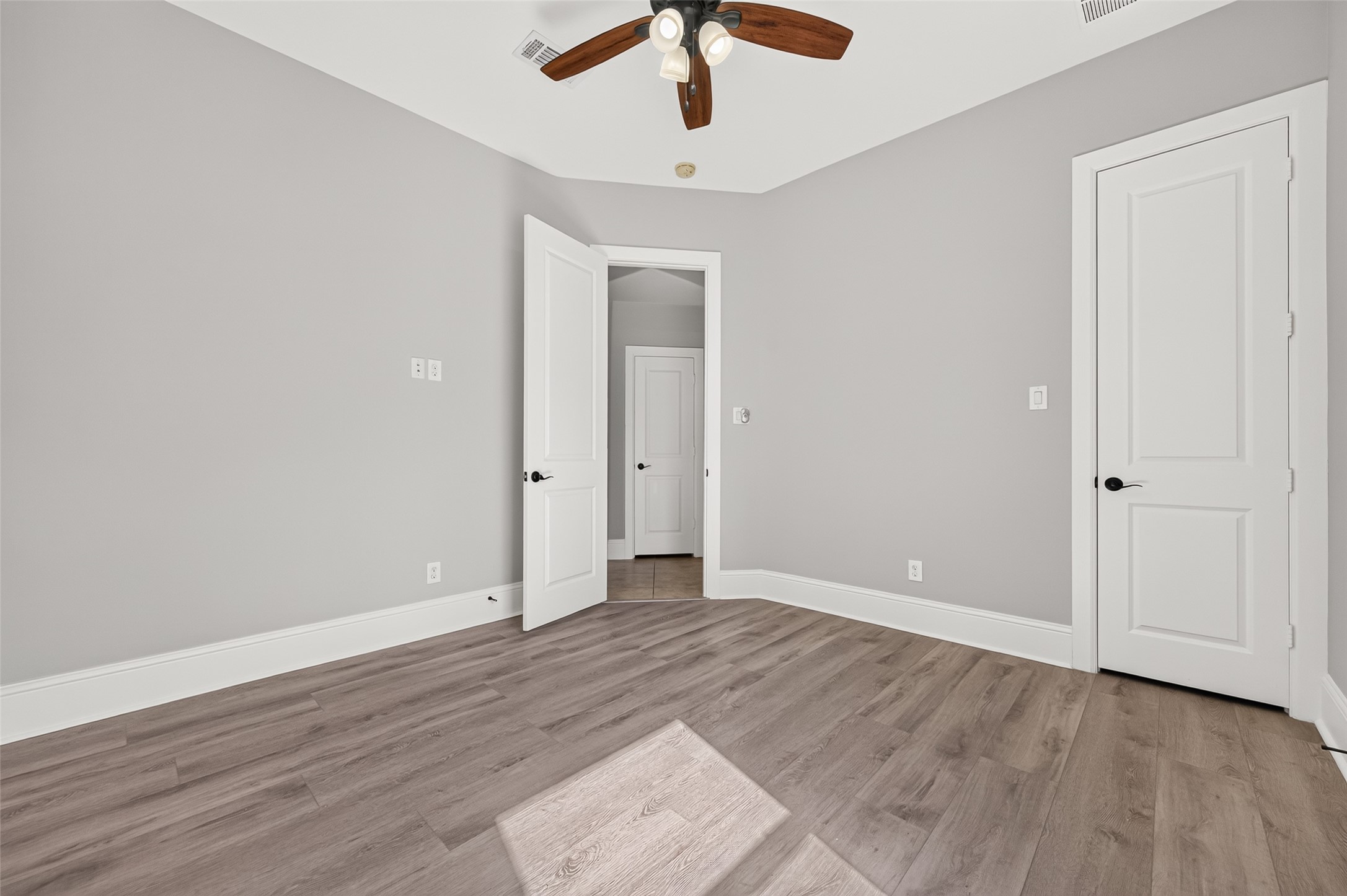 Versatile downstairs guest bedroom! Showcases a stunning rustic wood-plank accent wall, modern wood-look flooring, a stylish ceiling fan, and an arched window providing natural light and serene front-yard views.