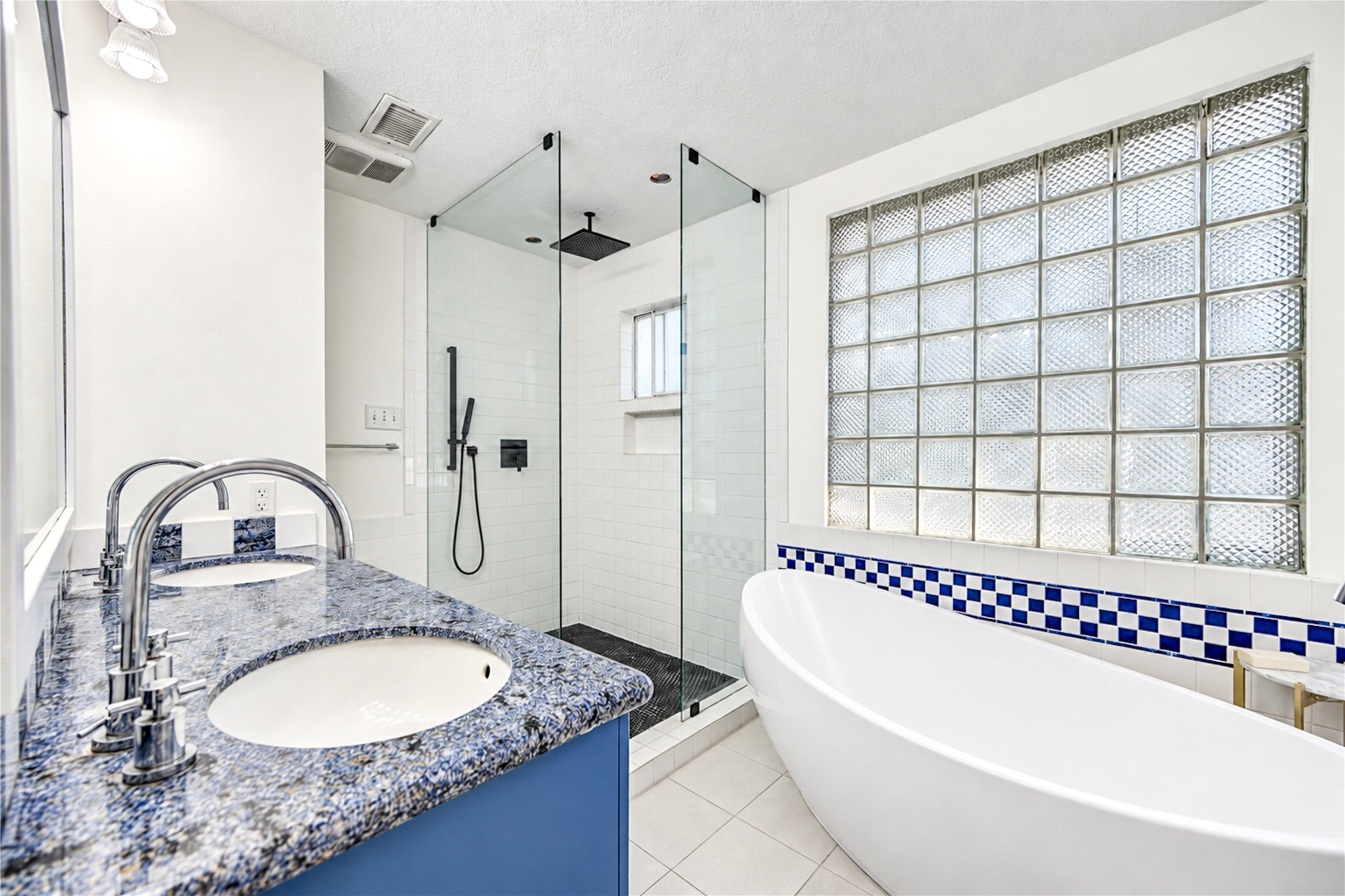 Indulge in a little everyday luxury! This beautifully renovated primary ensuite bath features a stunning freestanding soaking tub framed by glass block windows, creating a bright and relaxing retreat. The spacious walk-in shower with frameless glass enclosure, stylish tilework and striking blue accents adds a fresh designer touch. Whether starting your morning or unwinding after a long day, this spa-inspired sanctuary makes every moment feel special!