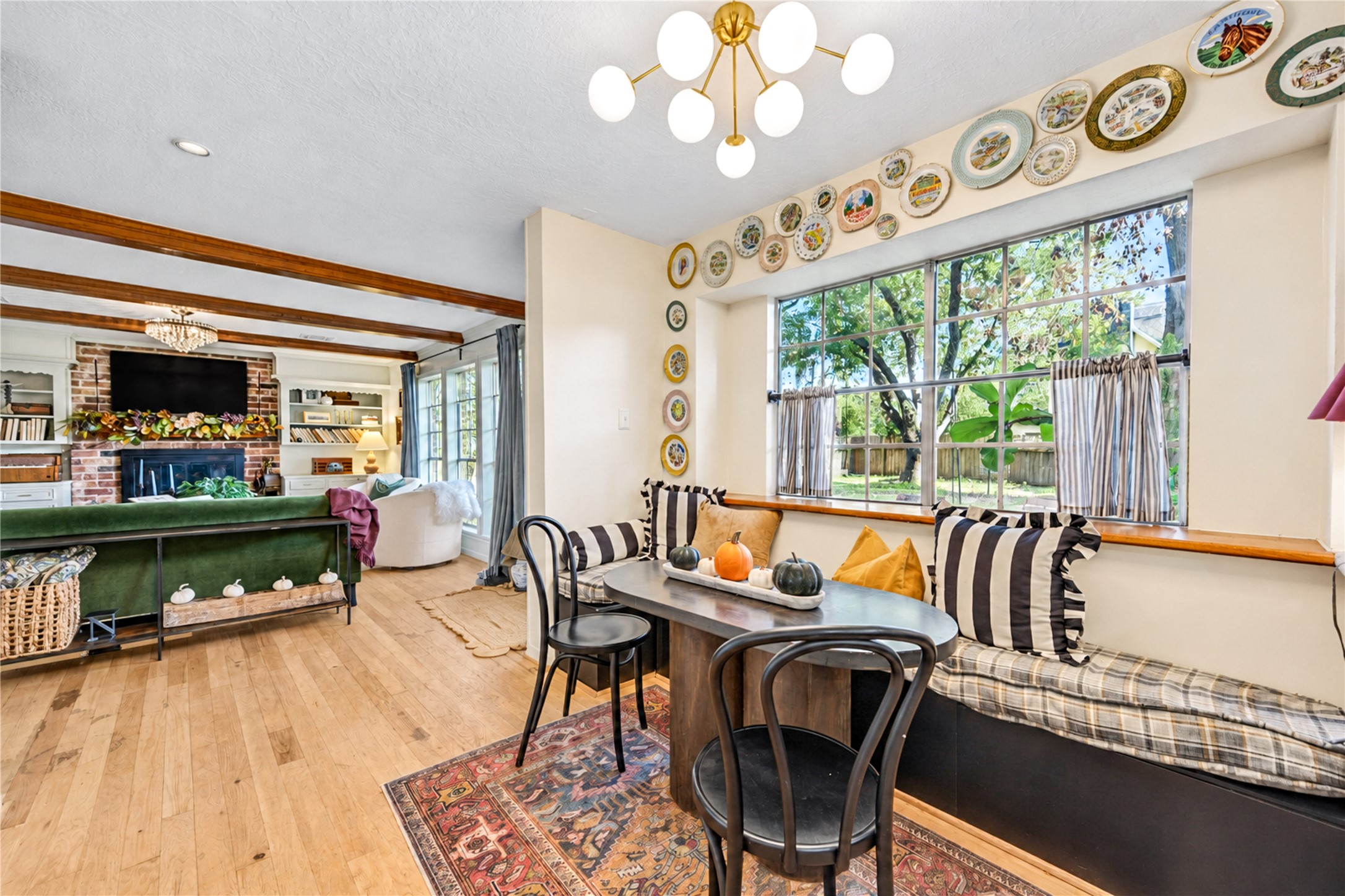 Start your mornings with sunshine and a cozy spot to linger! This charming breakfast room features a delightful built-in window seat overlooking the greenery outside, beautiful wood floors and a stylish statement chandelier. Thoughtful designer touches create a warm, inviting space perfect for sipping morning coffee, enjoying casual meals or curling up by the window with a favorite book. A little everyday luxury!