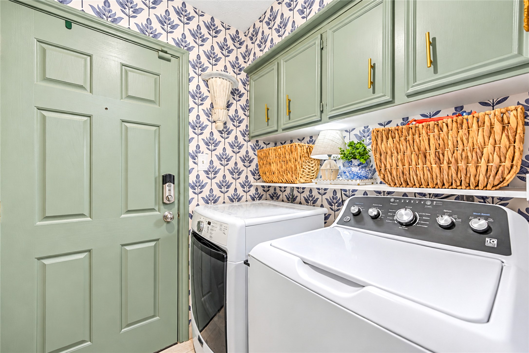 Who says laundry day can't be stylish? This cheerful first-floor laundry room brings personality to everyday chores with playful botanical wallpaper, soft sage-green cabinetry and a colorful patterned backsplash. Thoughtfully designed with generous countertop space for folding and upper cabinets for storage, this charming space proves that even the most practical rooms can be filled with designer flair!