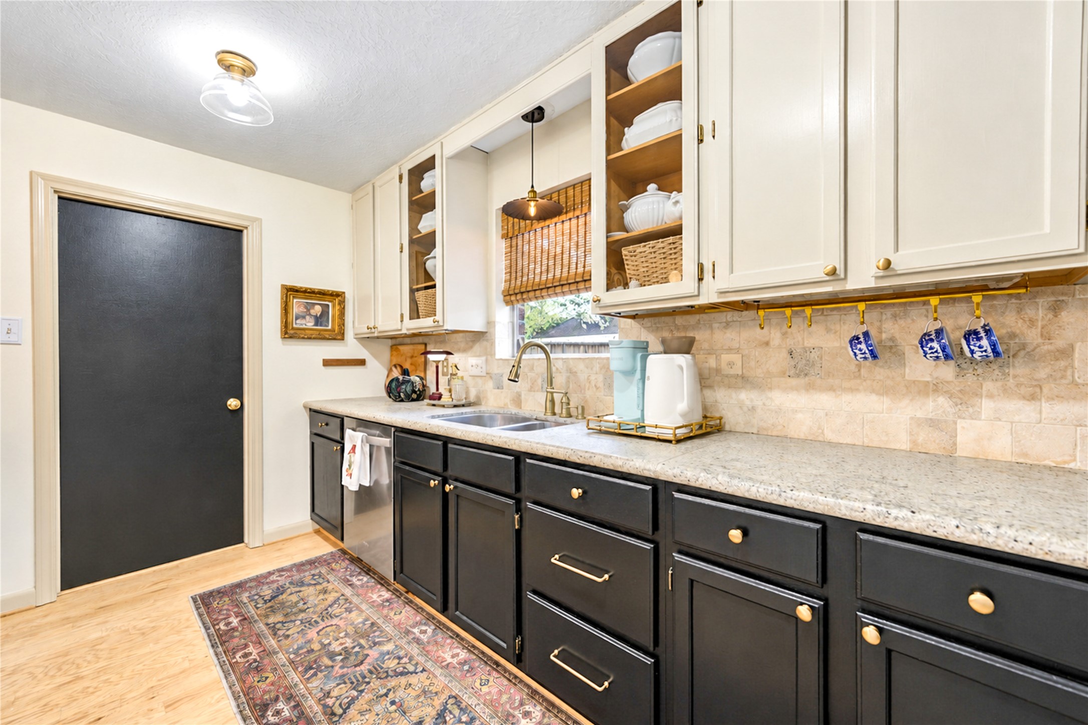 Style meets everyday convenience in this thoughtfully designed kitchen! Crisp white upper cabinetry contrasts beautifully with rich dark lower cabinets, while granite countertops and a travertine backsplash add timeless appeal. Charming display shelves, warm wood floors and designer lighting bring personality to the space, making everything from morning meal prep to evening entertaining a pleasure!