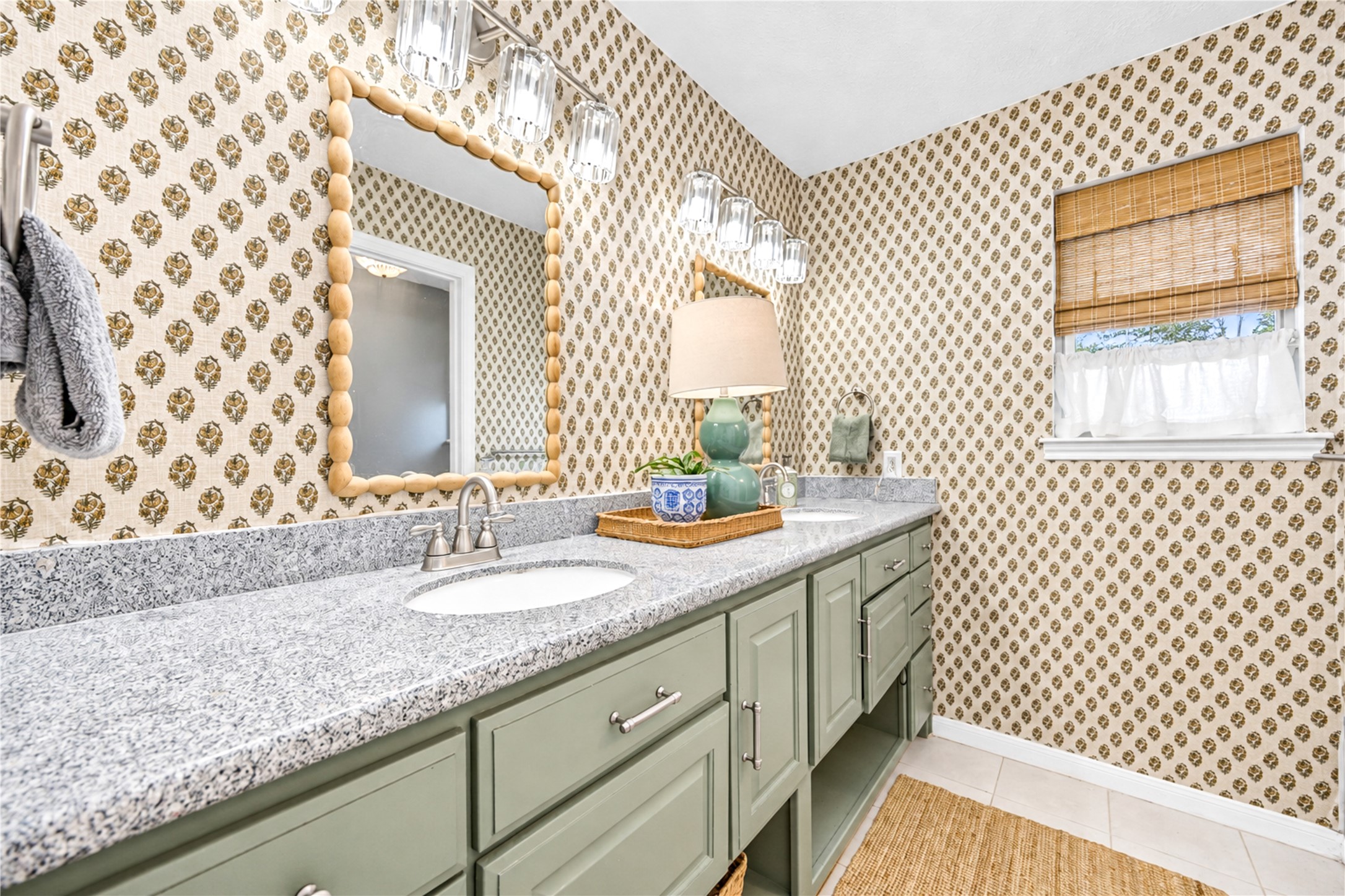 Designer charm continues into the second upstairs bathroom! A spacious vanity with soft sage-green cabinetry, decorative tile backsplash and a beautifully framed mirror creates a fresh, inviting atmosphere. Natural light filters through the window, while thoughtful finishes add warmth and personality. A stylish and functional space that makes everyday routines feel a little more special!