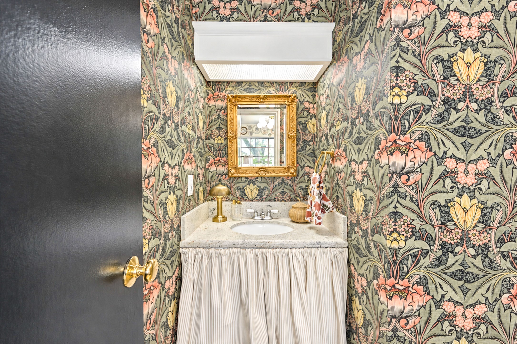 A little jewel box of designer style! This charming first-floor powder room makes a bold statement with its gorgeous botanical wallpaper, elegant framed mirror and classic pedestal sink with a tailored fabric skirt. Thoughtfully styled by the home's interior decorator owner, this delightful space adds a touch of personality and sophistication, making even the smallest room feel special!